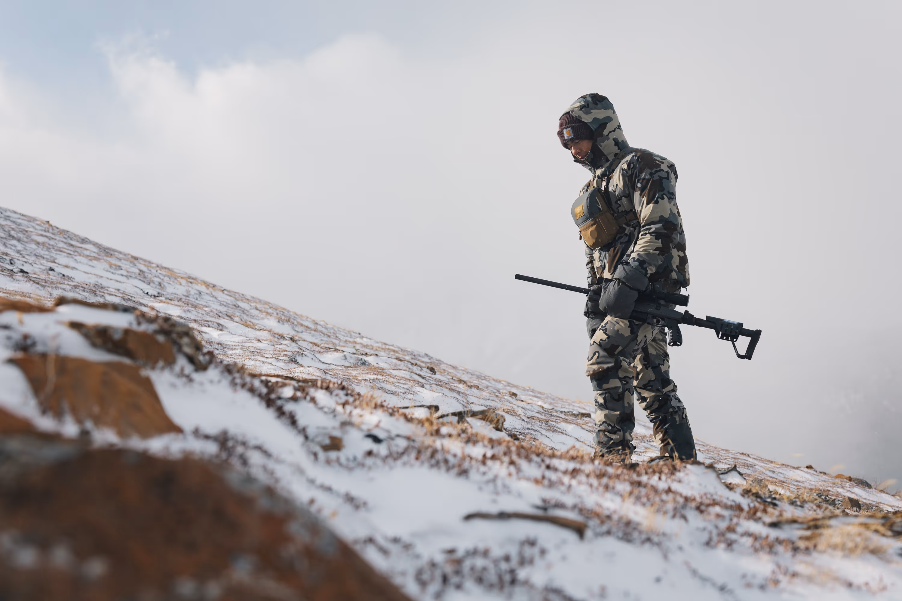 Hand opening a foaming can of Coors Banquet beer next to a fishing rod on a rock.