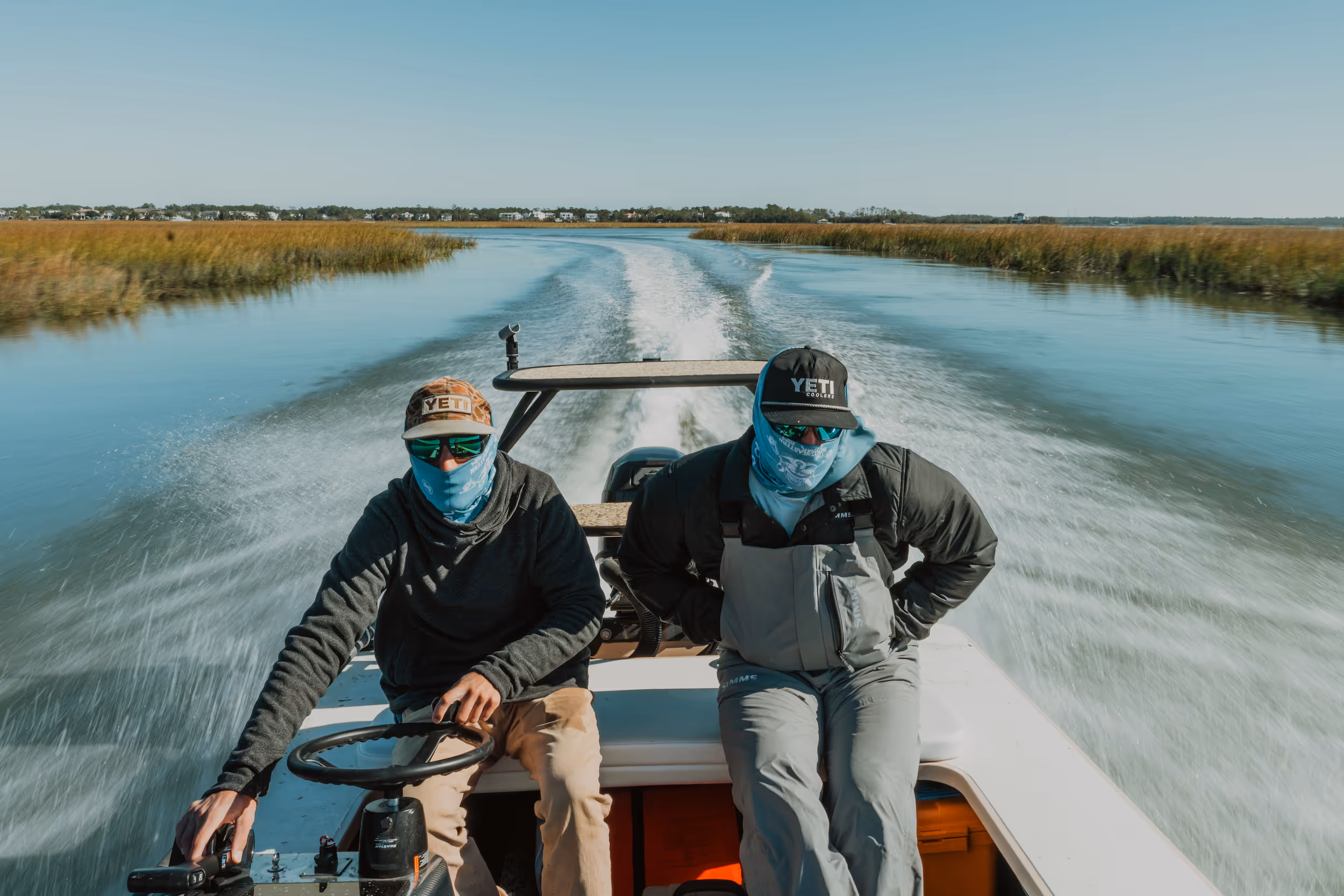 Close-up of a person wearing a textured blue Buff neck gaiter and sunglasses with sunlight in the background.