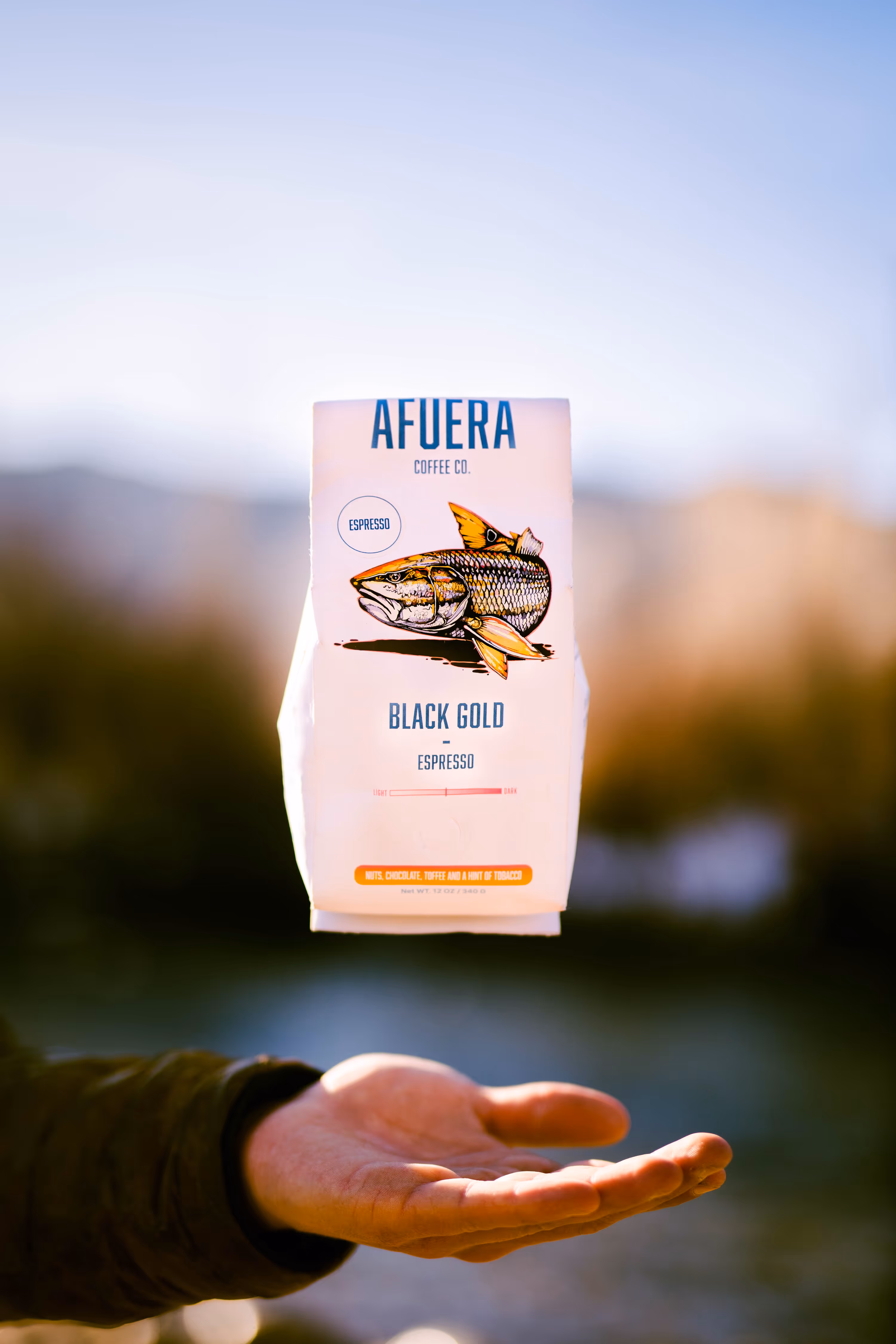 Hand holding a bag of Afuera Coffee Co. Black Gold espresso with fish illustration on the package.