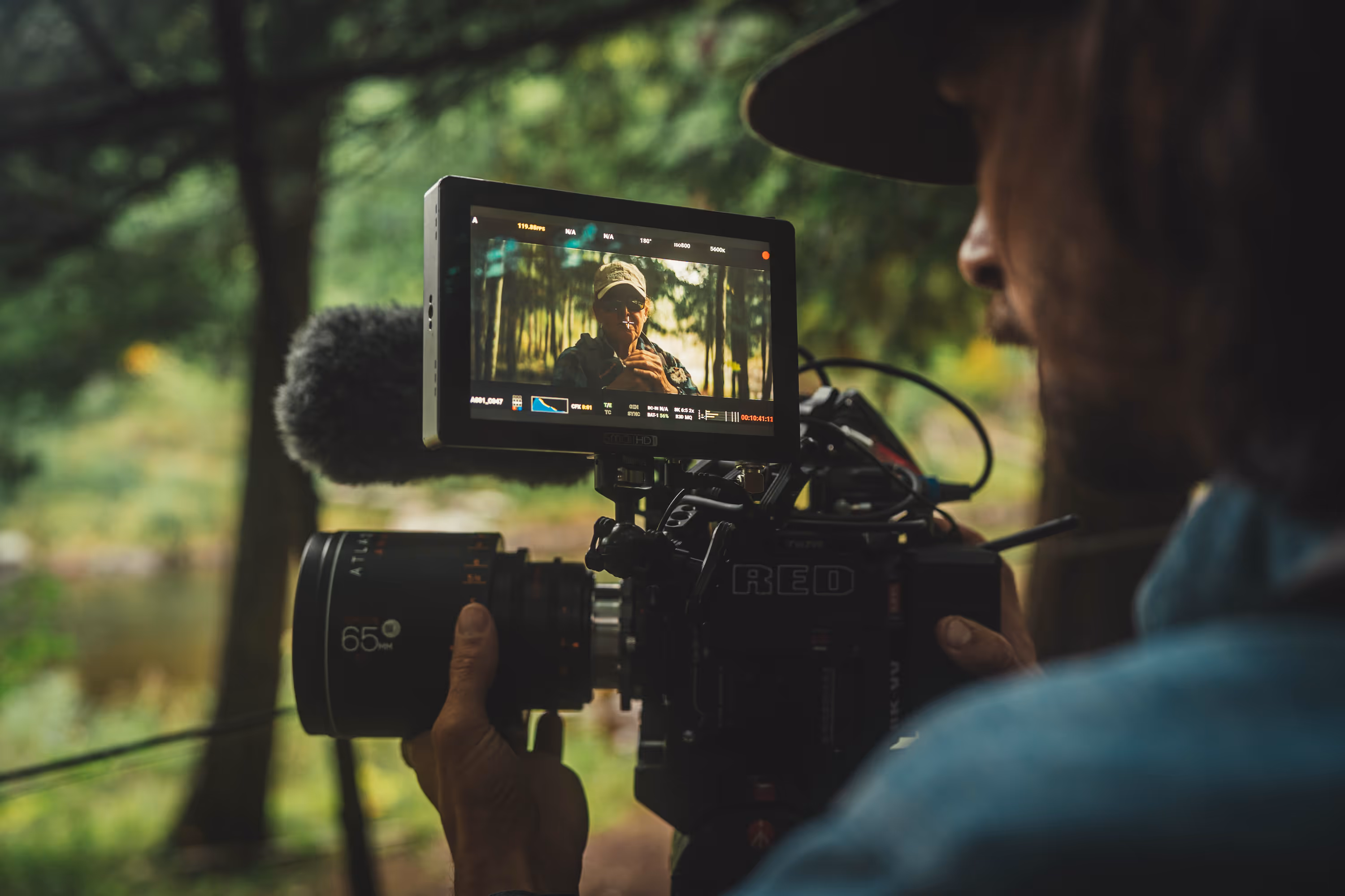 Man in a hoodie holding a fishing rod standing on a wooden pier overlooking a calm sea under a cloudy sky.