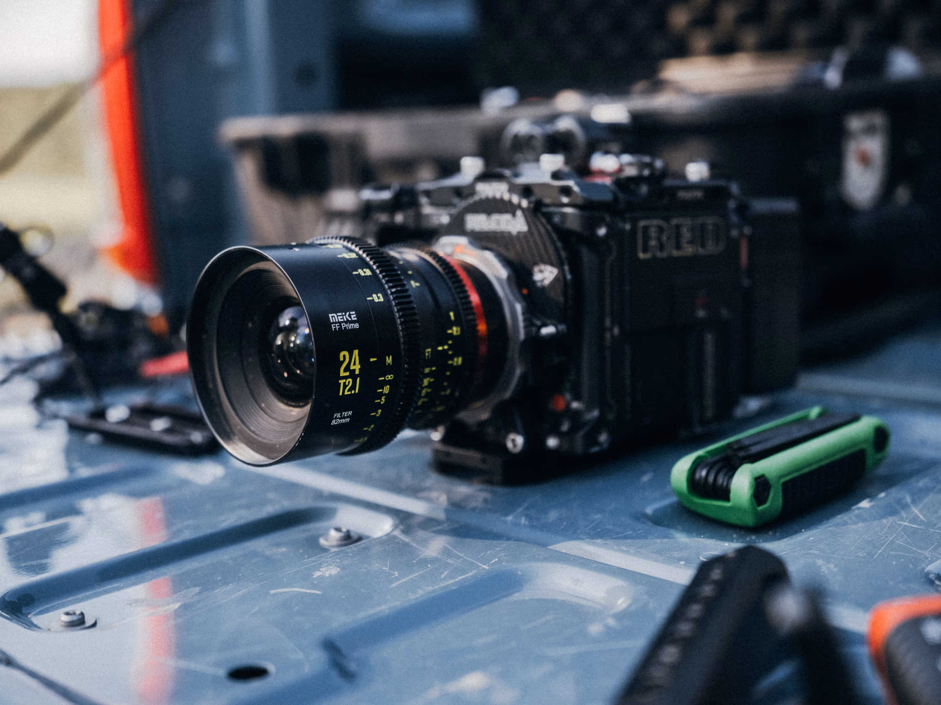 Close-up of a RED professional cinema camera with a Meike 24mm T2.1 lens on a gray metal surface, next to a green multi-tool.