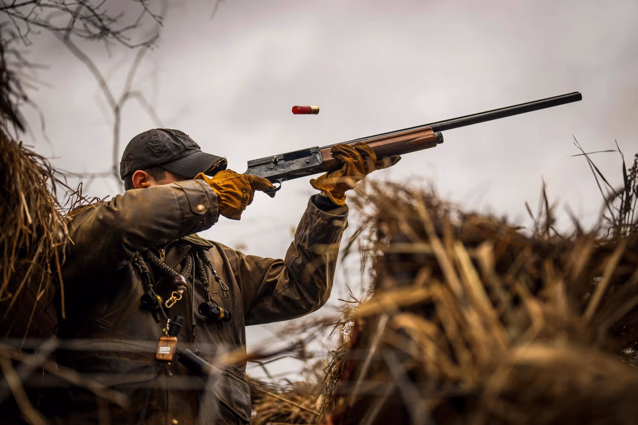 A man shooting a shotgun into the sky with a shell being ejected out the side