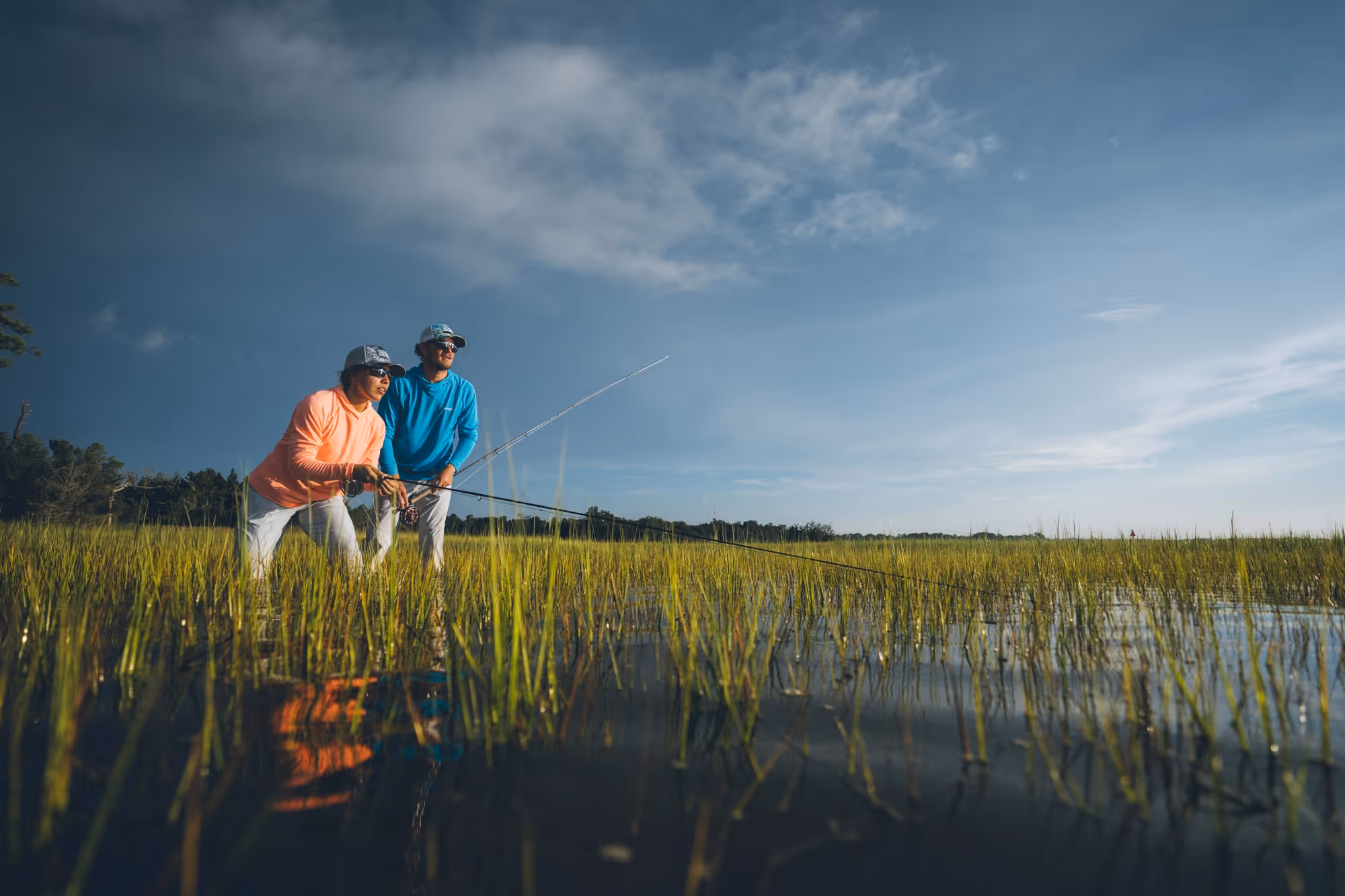A woman holding a fly rod and a guide standing next to her looking out over a flood plain