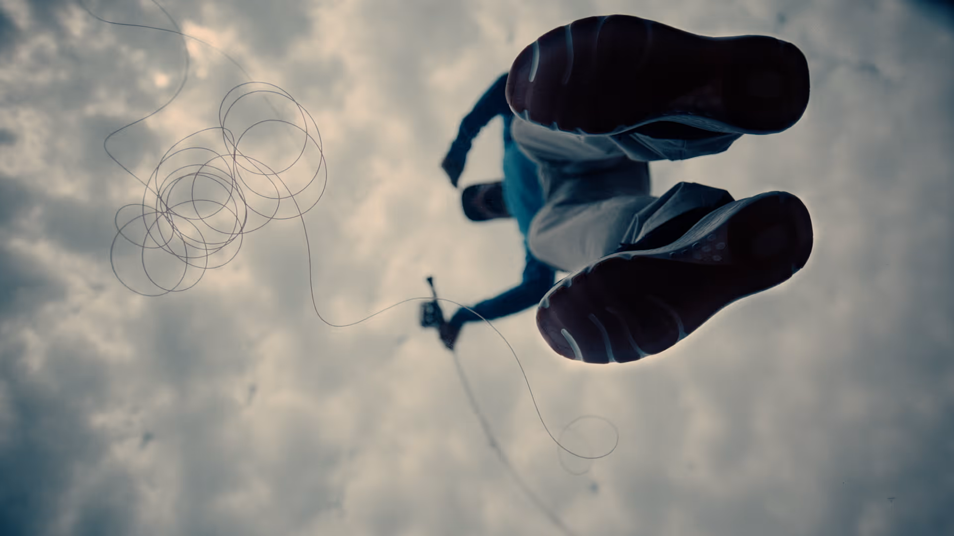 Two people wearing camouflage jackets and waders standing back-to-back in shallow water, one holding a fishing rod and the other a camouflaged rifle.