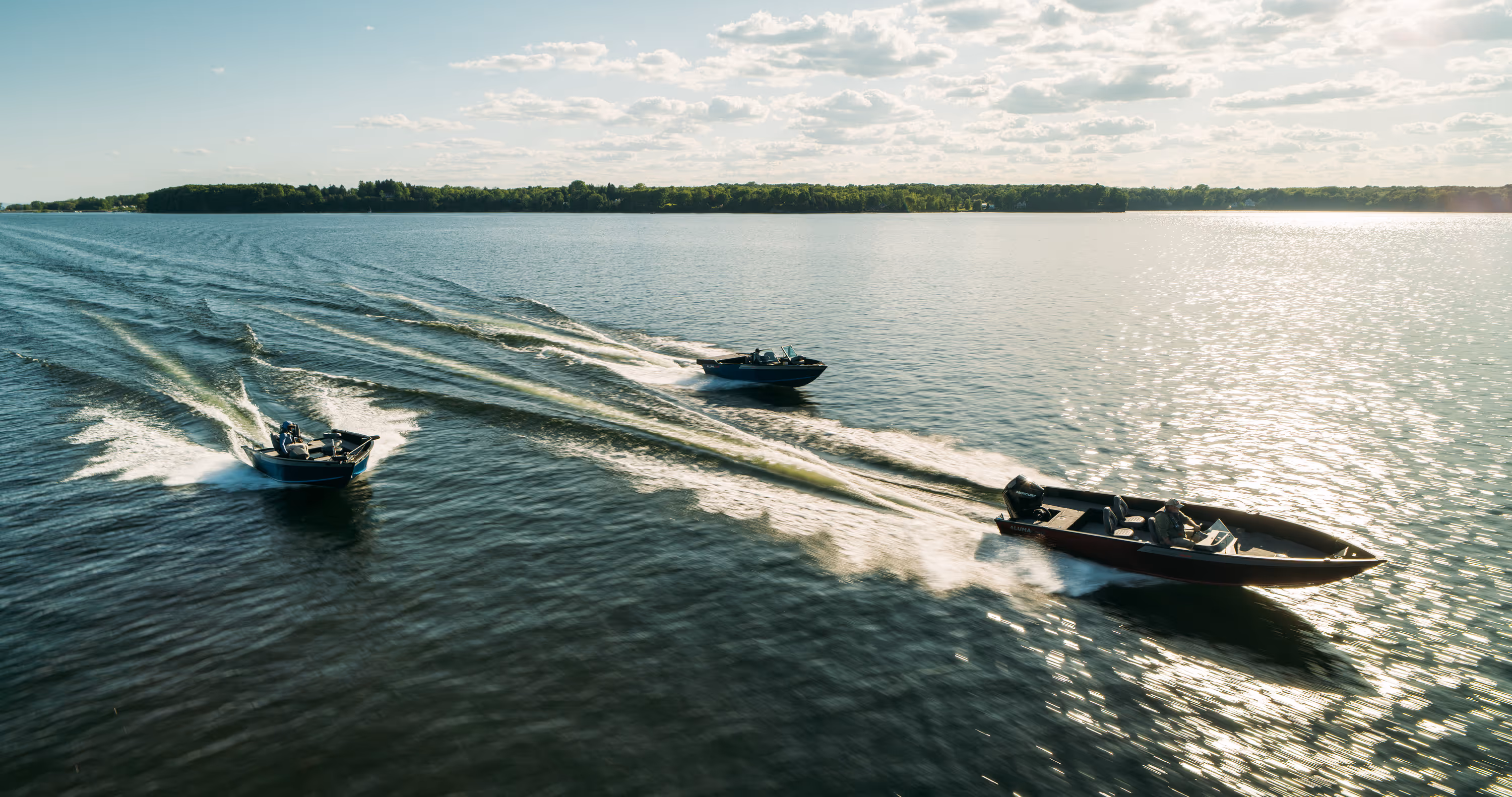 Two people wearing camouflage jackets and waders standing back-to-back in shallow water, one holding a fishing rod and the other a camouflaged rifle.