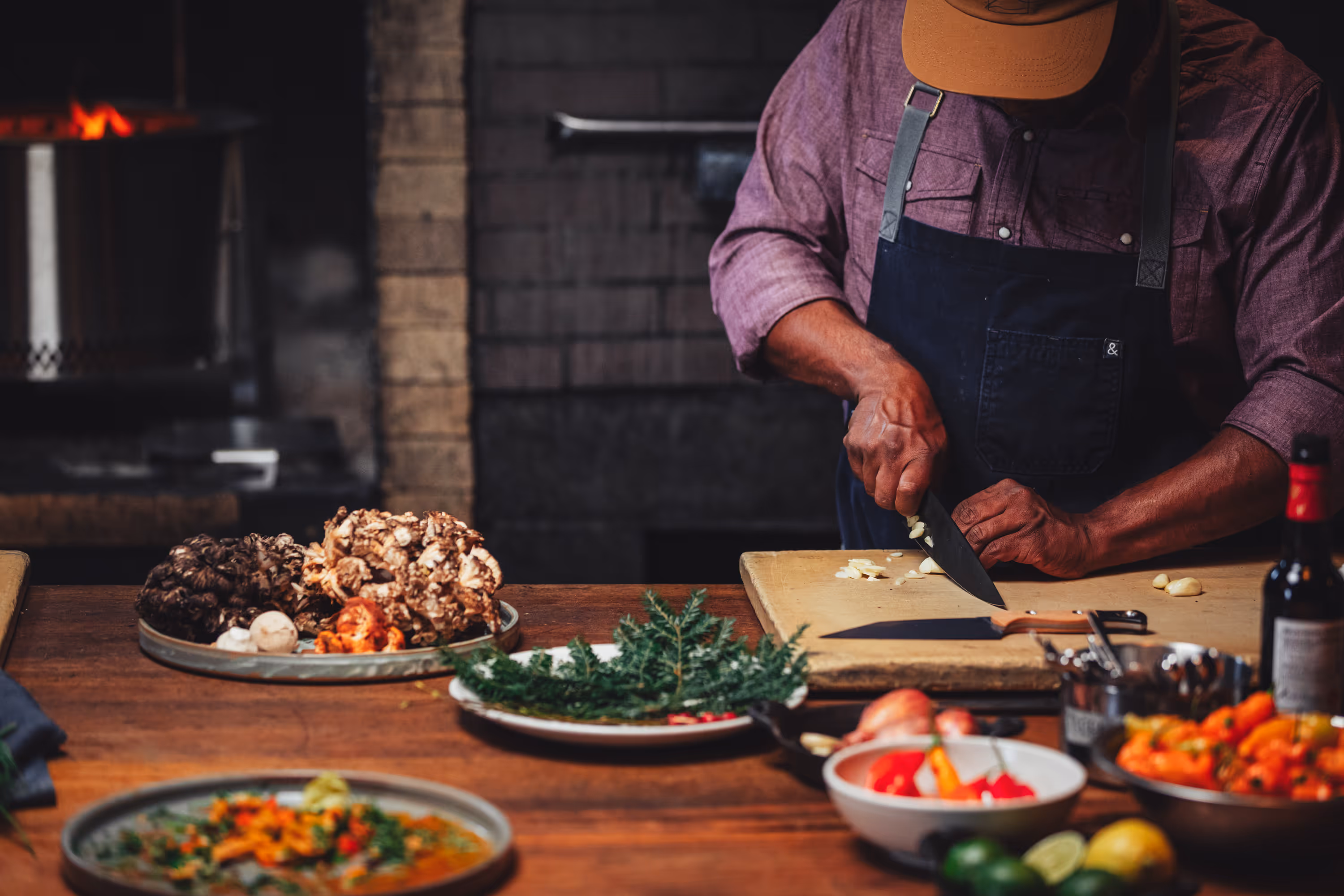 Two people wearing camouflage jackets and waders standing back-to-back in shallow water, one holding a fishing rod and the other a camouflaged rifle.