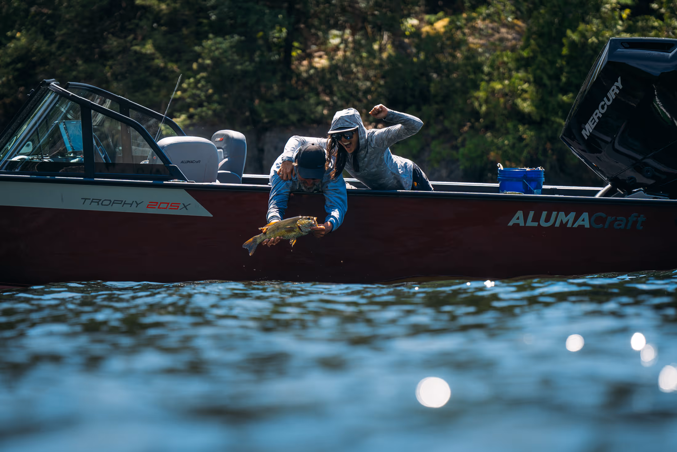 A man and woman hanging over the edge of a alumacraft boat holding a bass