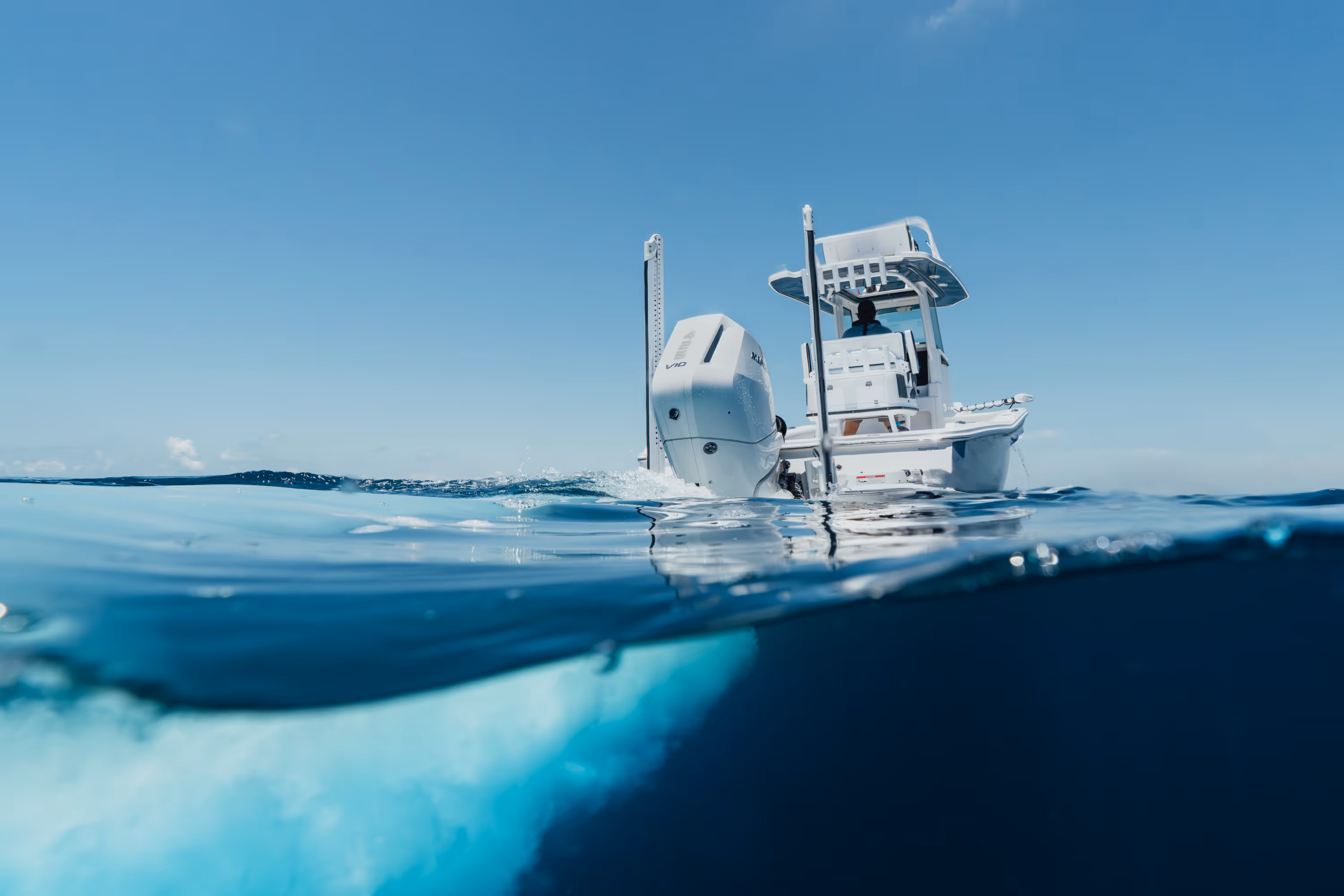 Two people wearing camouflage jackets and waders standing back-to-back in shallow water, one holding a fishing rod and the other a camouflaged rifle.