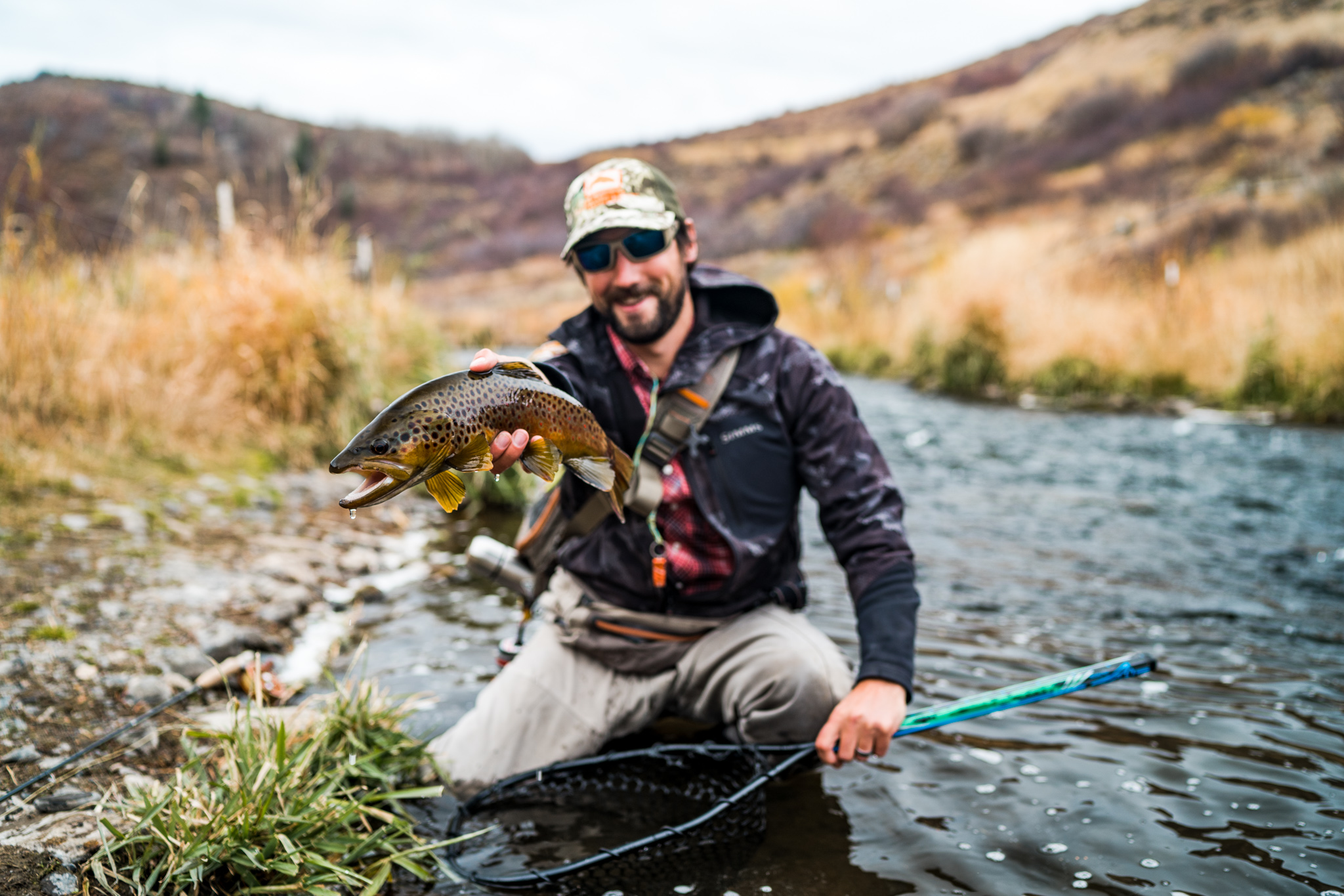 Man holding a brown trout while kneeling next to a river