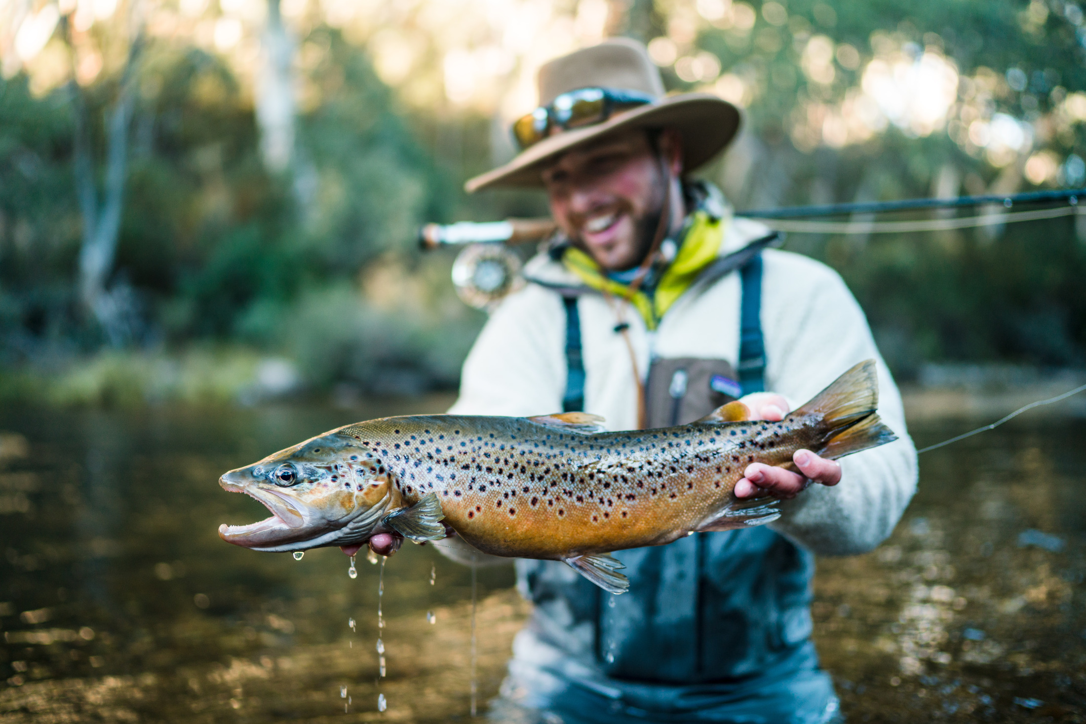 man holding a large brown trout dripping water while standing in a river 