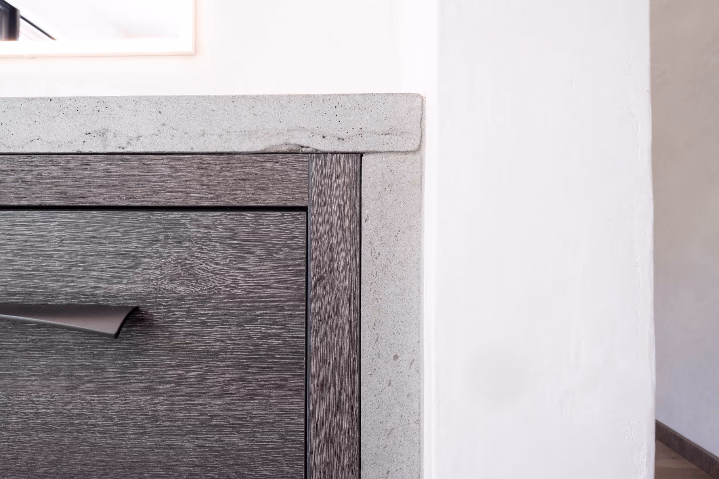 Close-up of a modern dark wood drawer with a sleek black handle next to a light gray stone countertop and white wall.