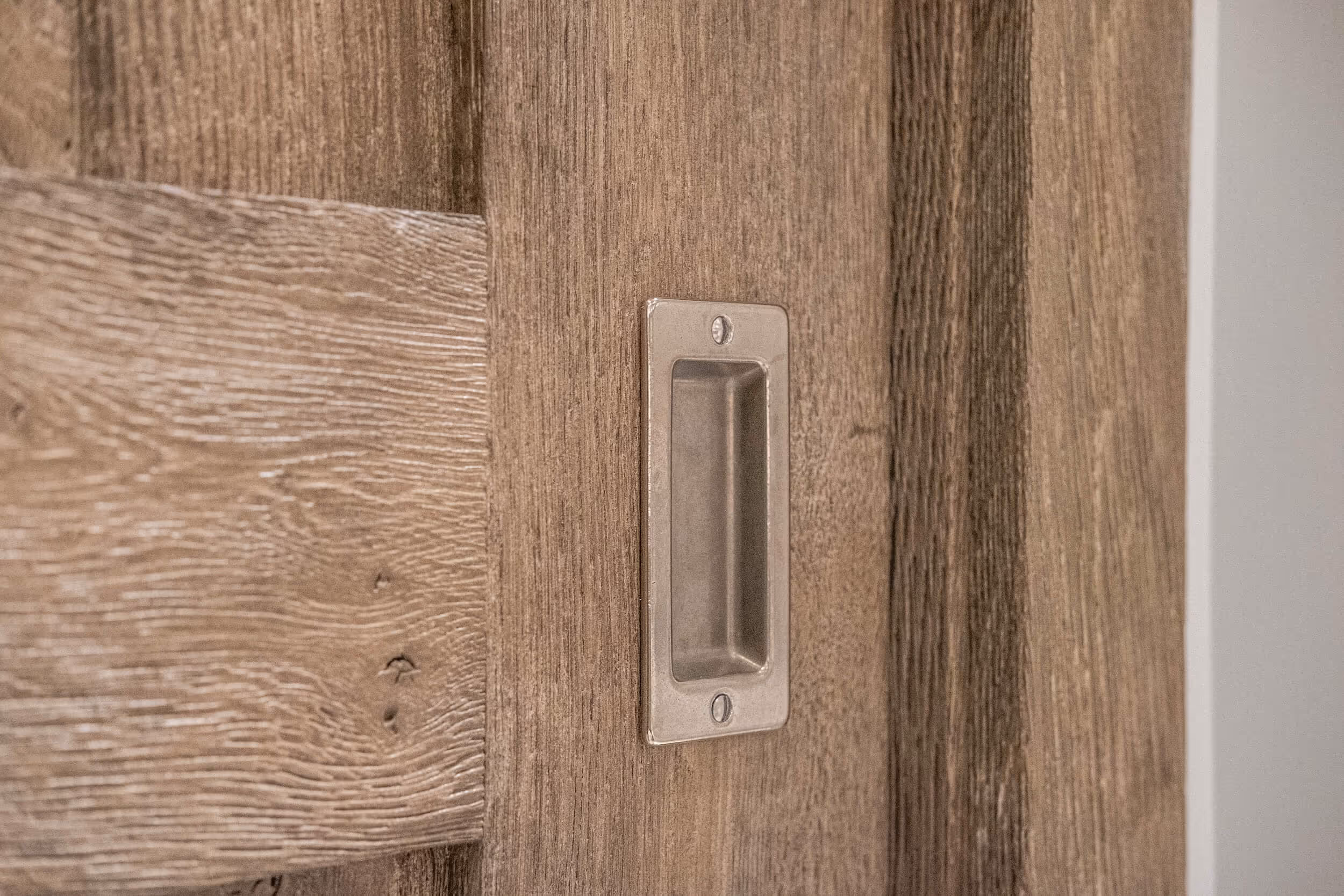 Recessed metal handle on a wooden sliding door with natural wood grain.