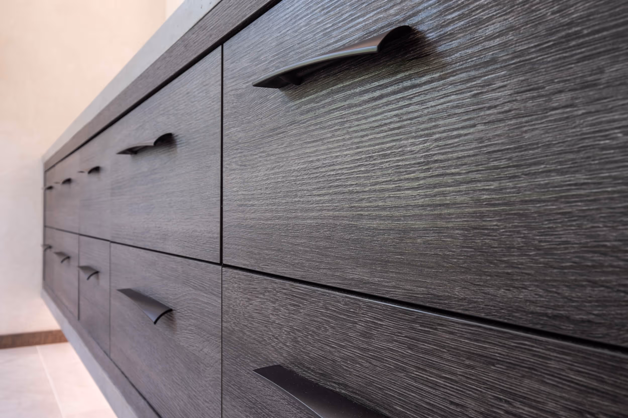Close-up side view of a modern dark wood cabinet with multiple drawers and sleek black handles.