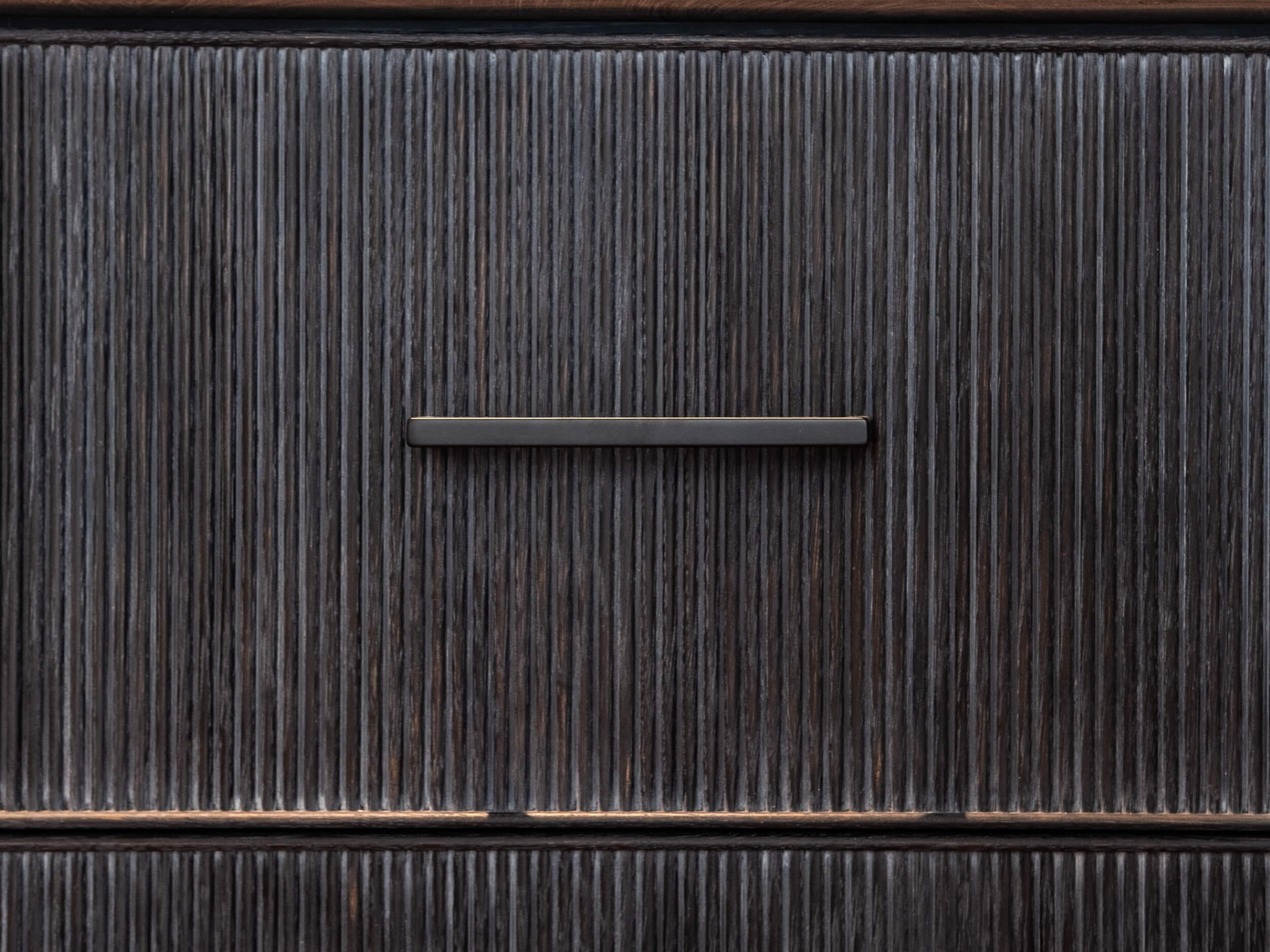 Dark wooden cabinet door with vertical grooves and a horizontal metal handle in the center.