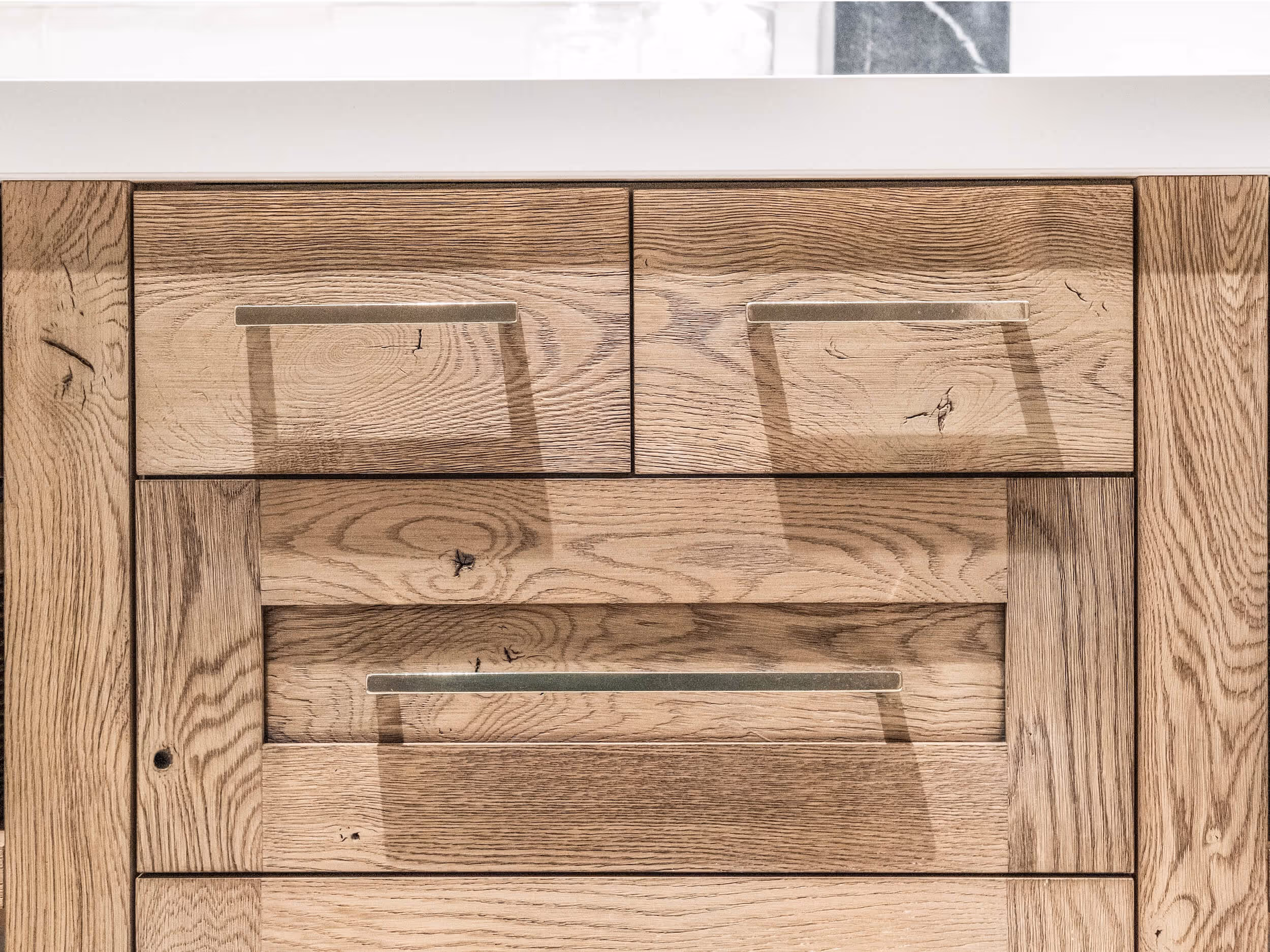 Close-up of wooden cabinet drawers with metal handles under a white countertop.