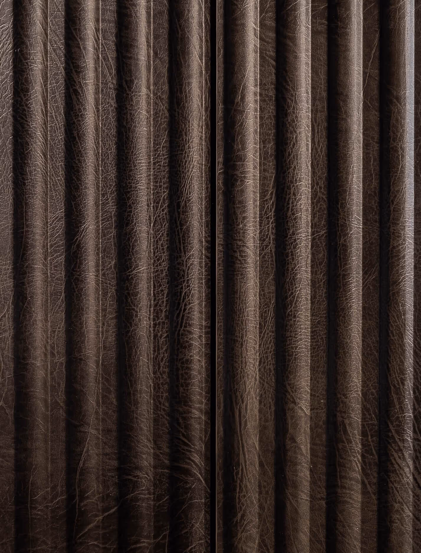 Close-up of dark brown, textured leather curtain with vertical folds and fine wrinkles.