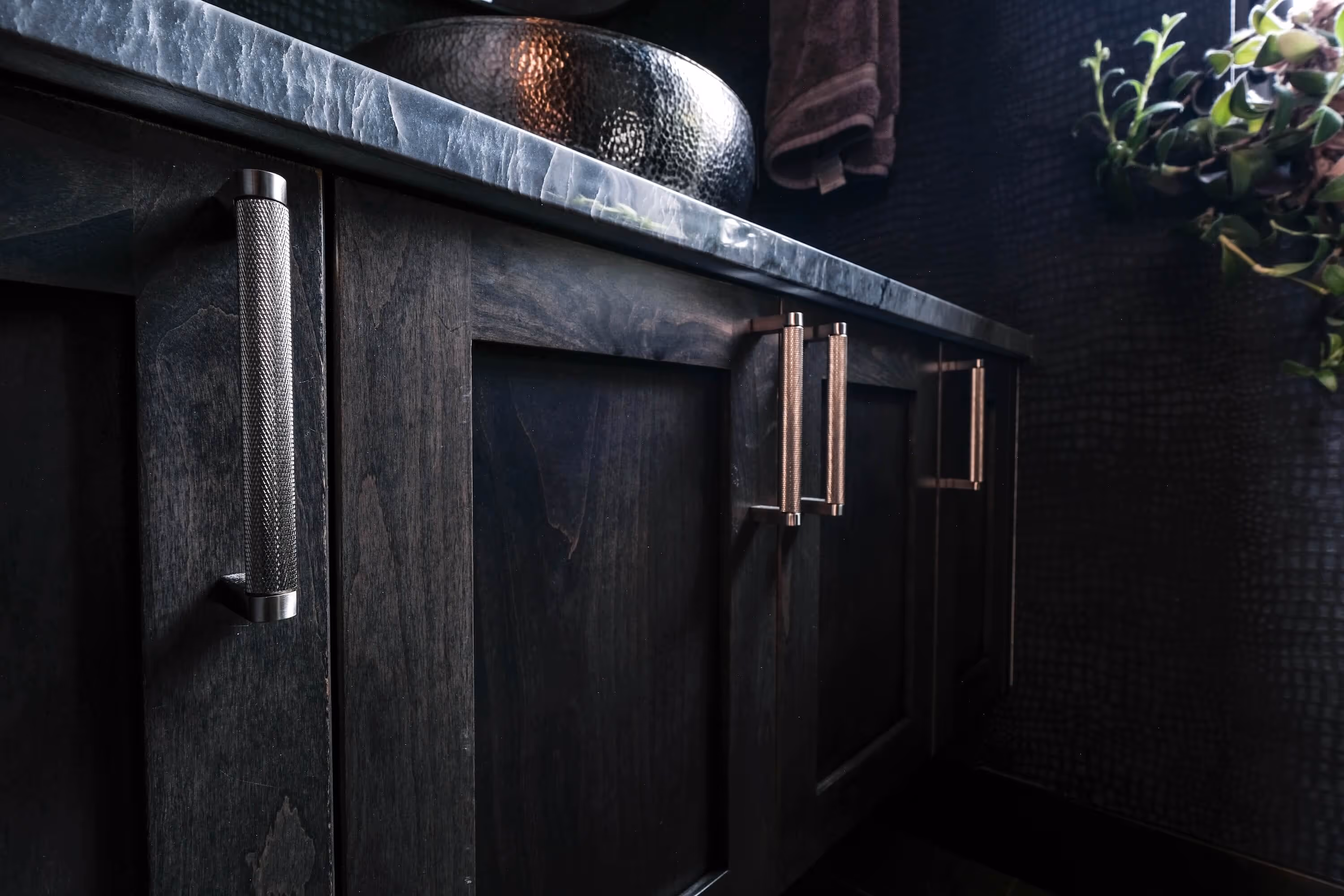 Modern bathroom with double sinks, illuminated mirrors, wood cabinetry, and a view of a comfortable armchair in an adjacent room.
