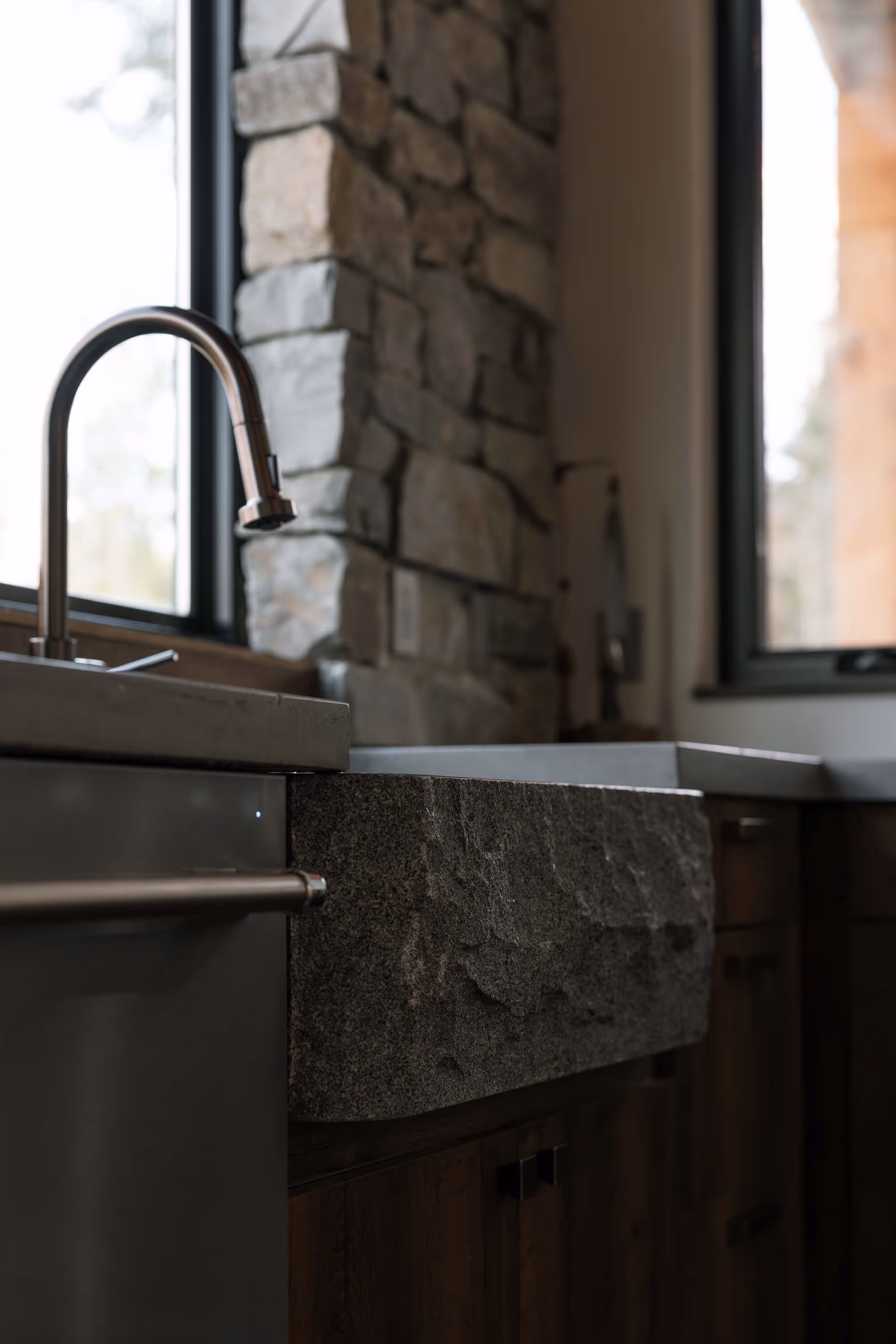 Modern kitchen sink with a rough stone apron, stainless steel faucet, and stone wall backdrop.