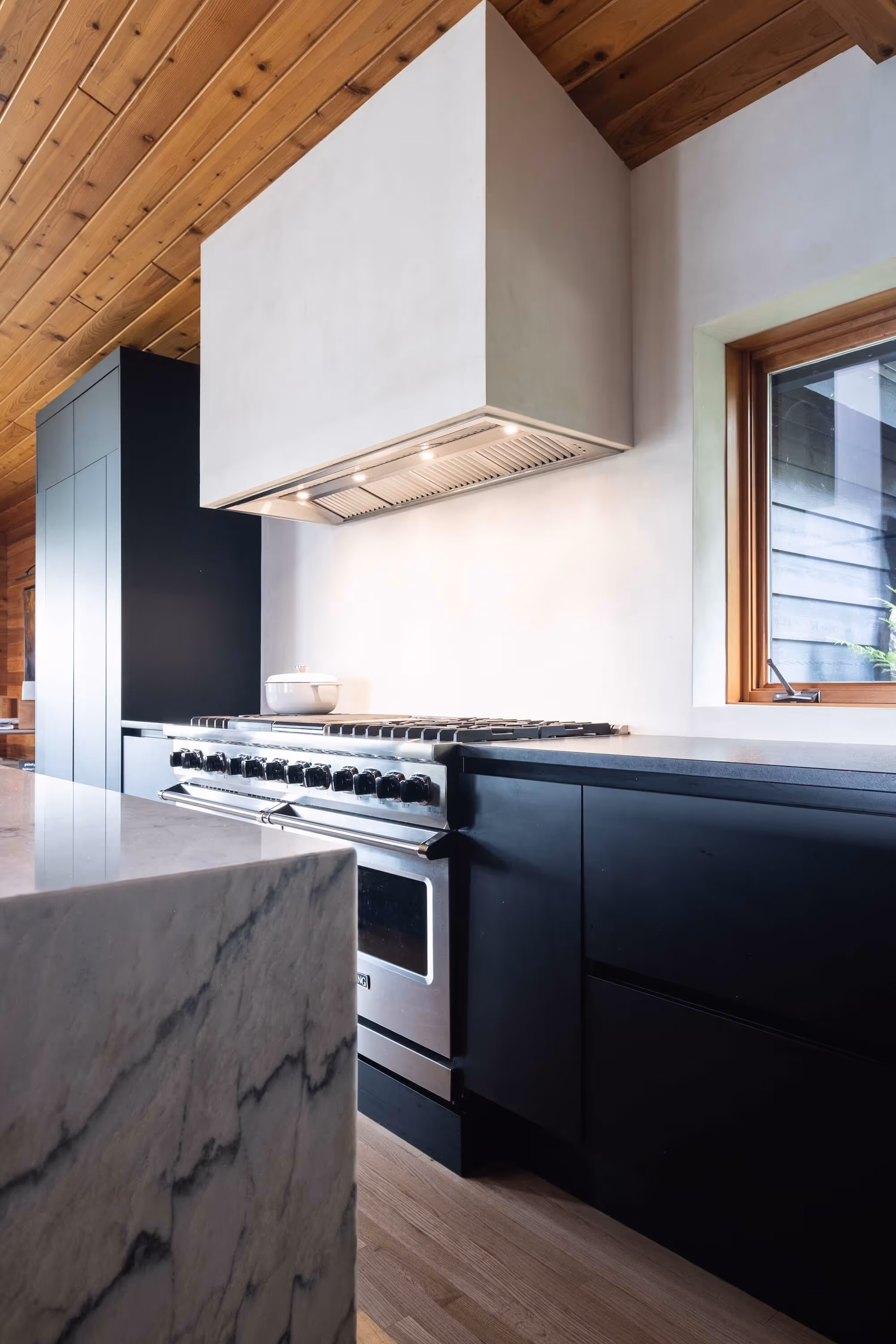 Modern kitchen with a stainless steel gas stove, black cabinetry, a marble countertop, and wooden ceiling and floor.