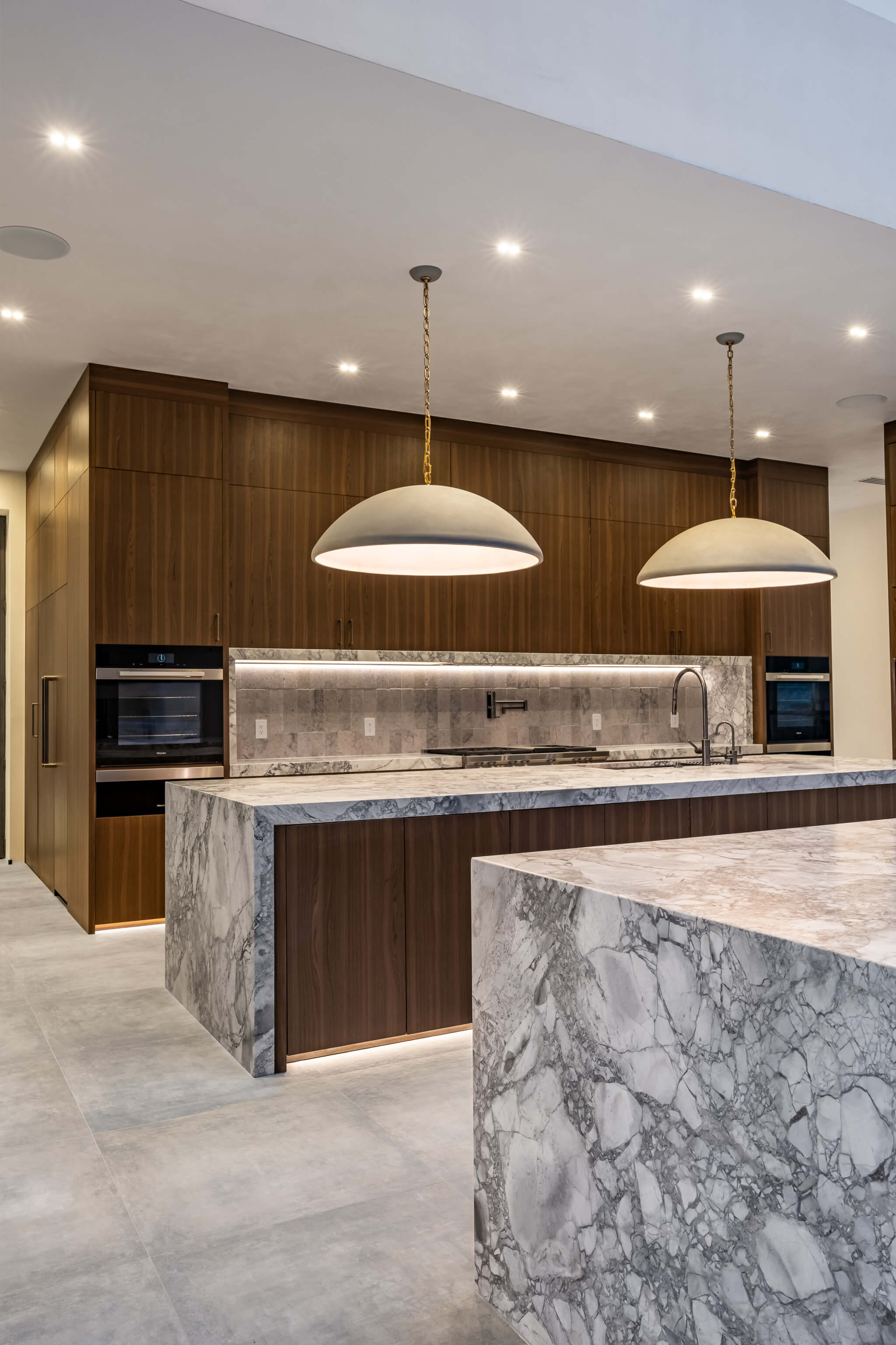 Modern kitchen sink with a curved faucet set in a concrete countertop beside large windows showing an outdoor wooded scene.