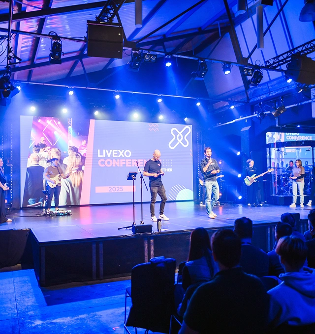 Speakers and musicians on stage at the Livexo Conference 2025 with an audience watching.