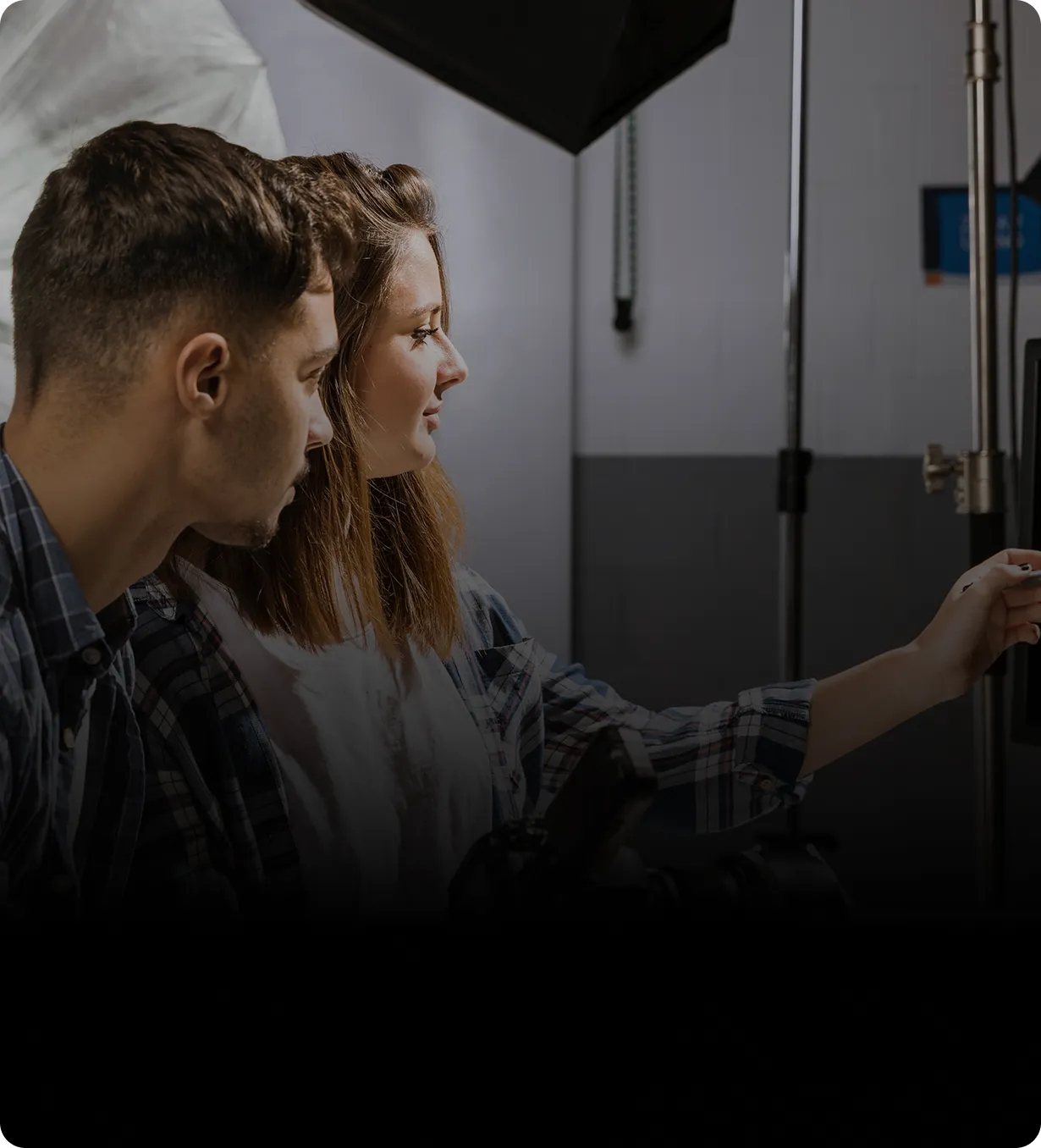 Two people, a man and a woman, look intently at a screen while the woman points at it in a studio setting.