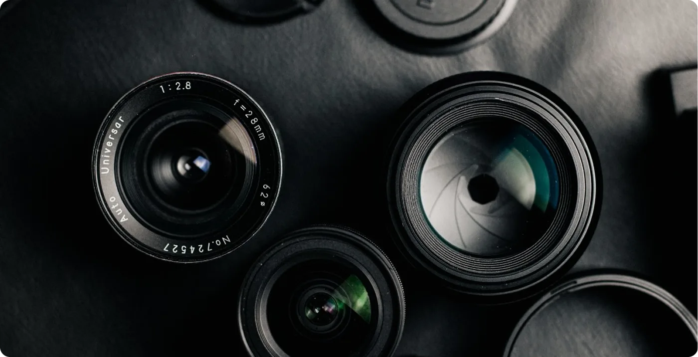 Three black camera lenses of different sizes arranged on a dark surface.