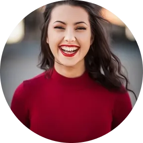 Young woman with long dark hair wearing a red top smiling brightly outdoors.