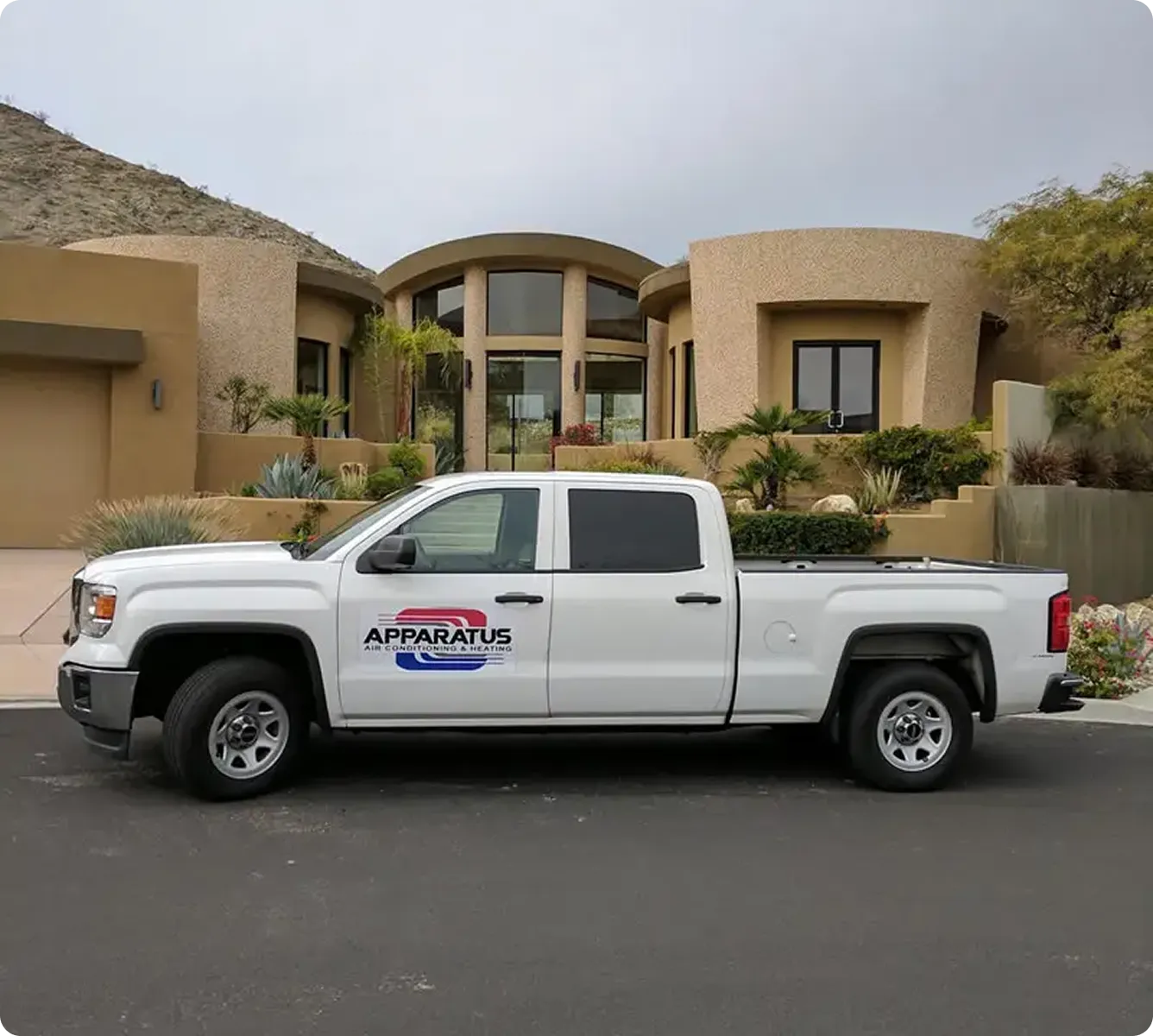 A white truck with the Apparatus logo parked outside a modern home with desert landscaping.