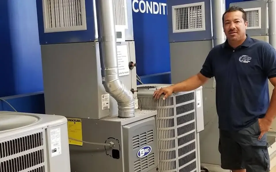 A technician stands beside air conditioning units, demonstrating equipment in a service center.
