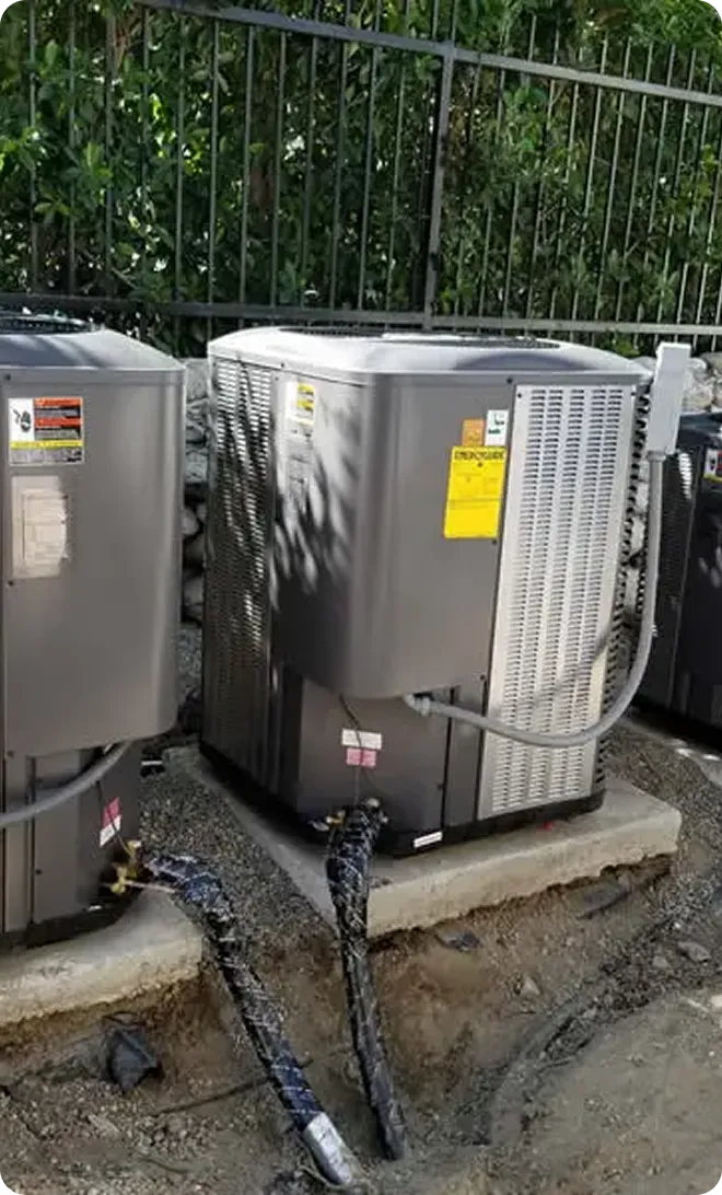 Two air conditioning units installed on a concrete pad, featuring visible pipes and gauges.