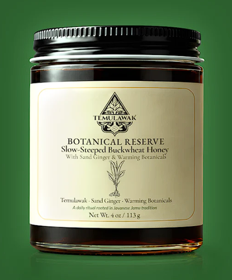 Open glass vessel of slow-fermenting Jamu Honey with gold-flecked surface, in warm directional light.