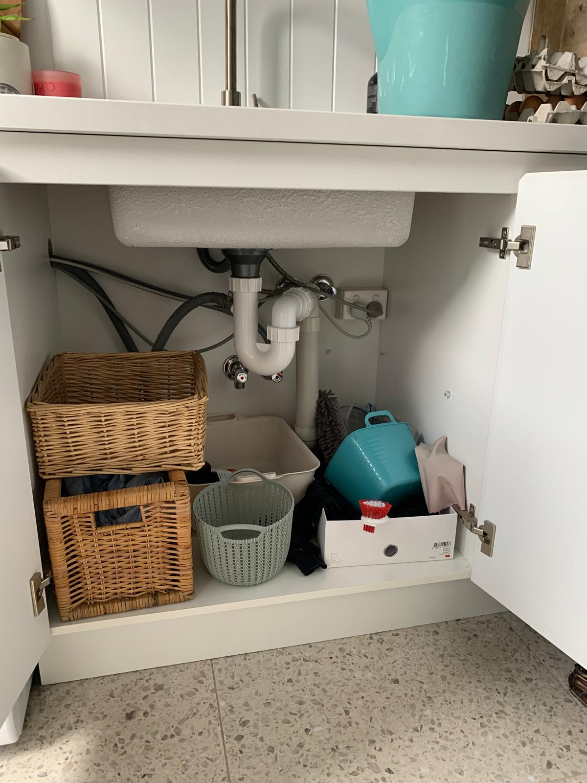 Bathroom cabinet interior with wicker baskets, sink pipes, and storage containers