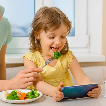 child on tablet eating broccoli
