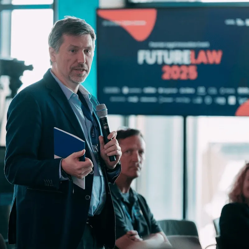 dr Paweł Kowalski w garniturze trzyma mikrofon i notatnik podczas prezentacji na konferencji Future Law 2025.