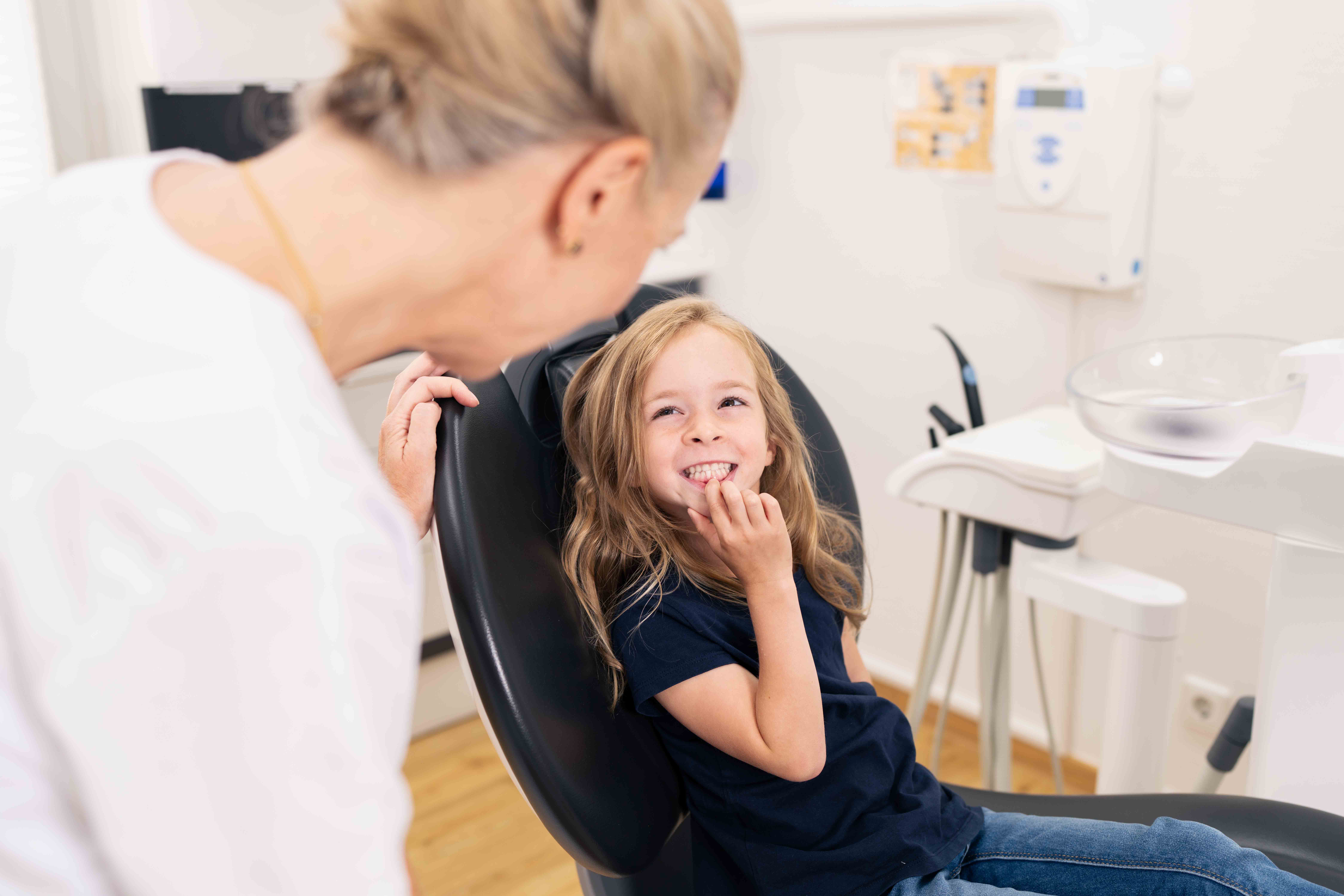 Smiling young girl sitting in a dental chair looking at a female dentist in a bright dental office.