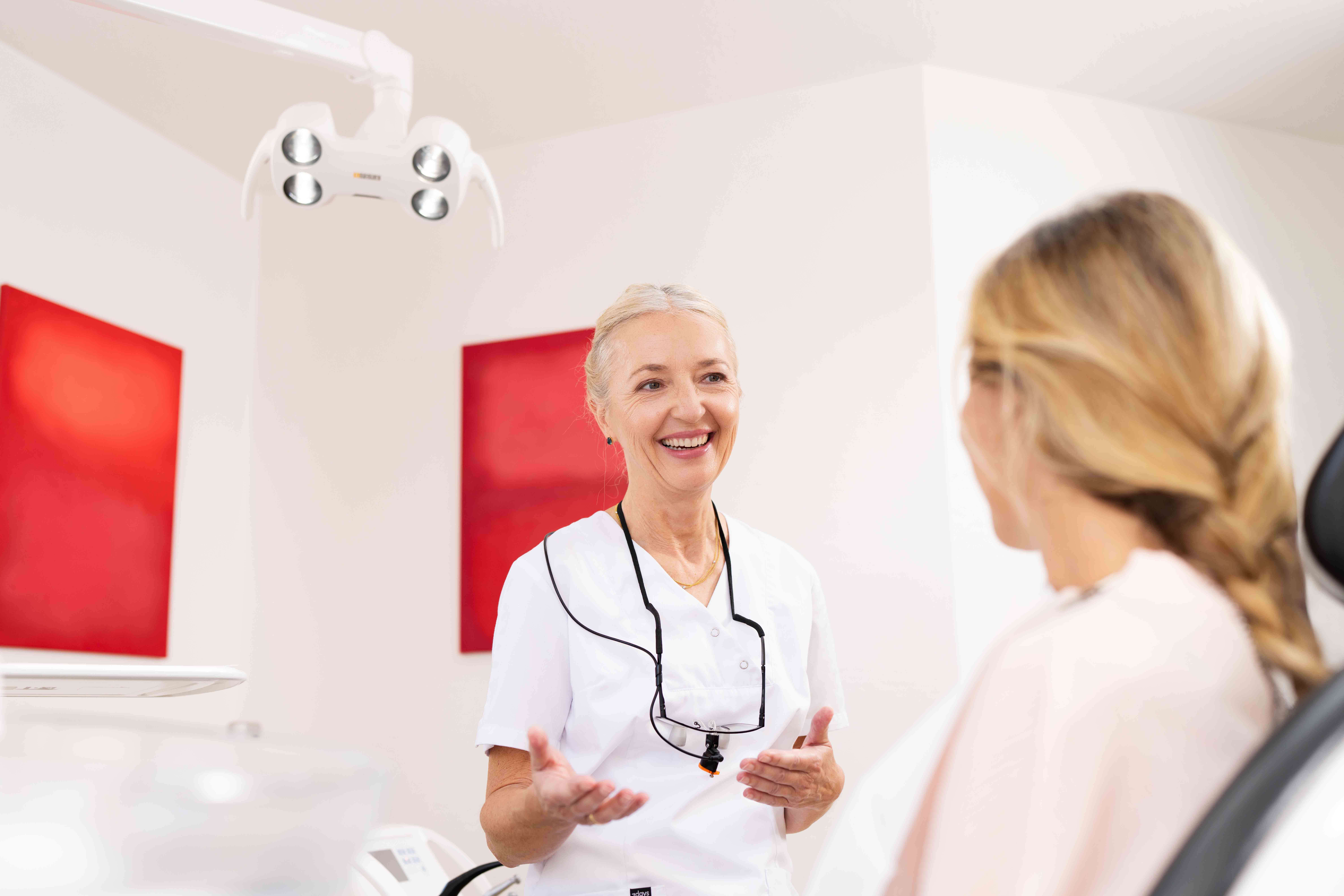 Smiling female dentist talking to a patient in a dental office with red artwork on the walls.