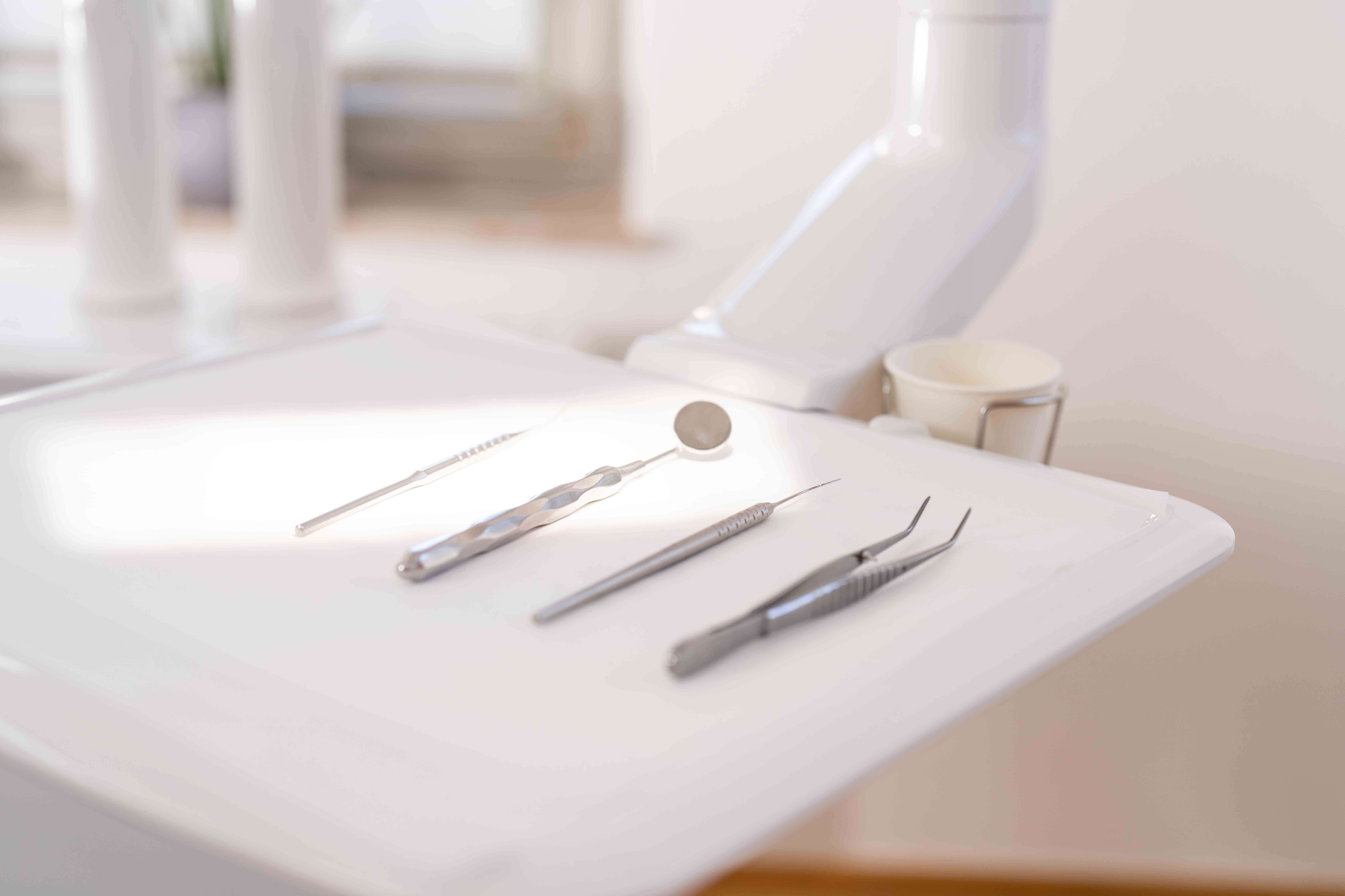 Dental tools including a mirror, scaler, probe, and tweezers arranged on a white tray in a dental office.