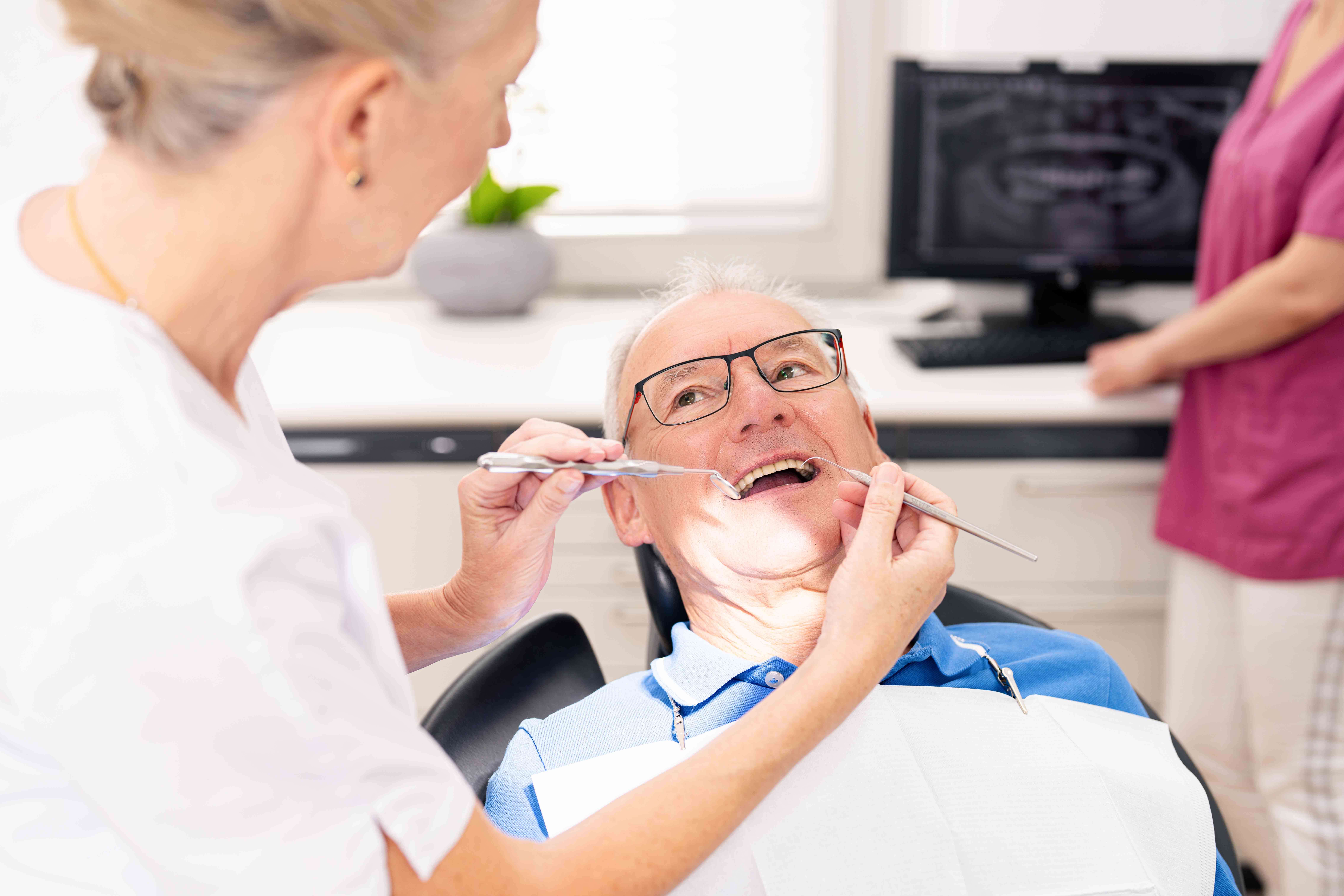 Dentist examining an elderly male patient's teeth during a dental checkup in a clinic.
