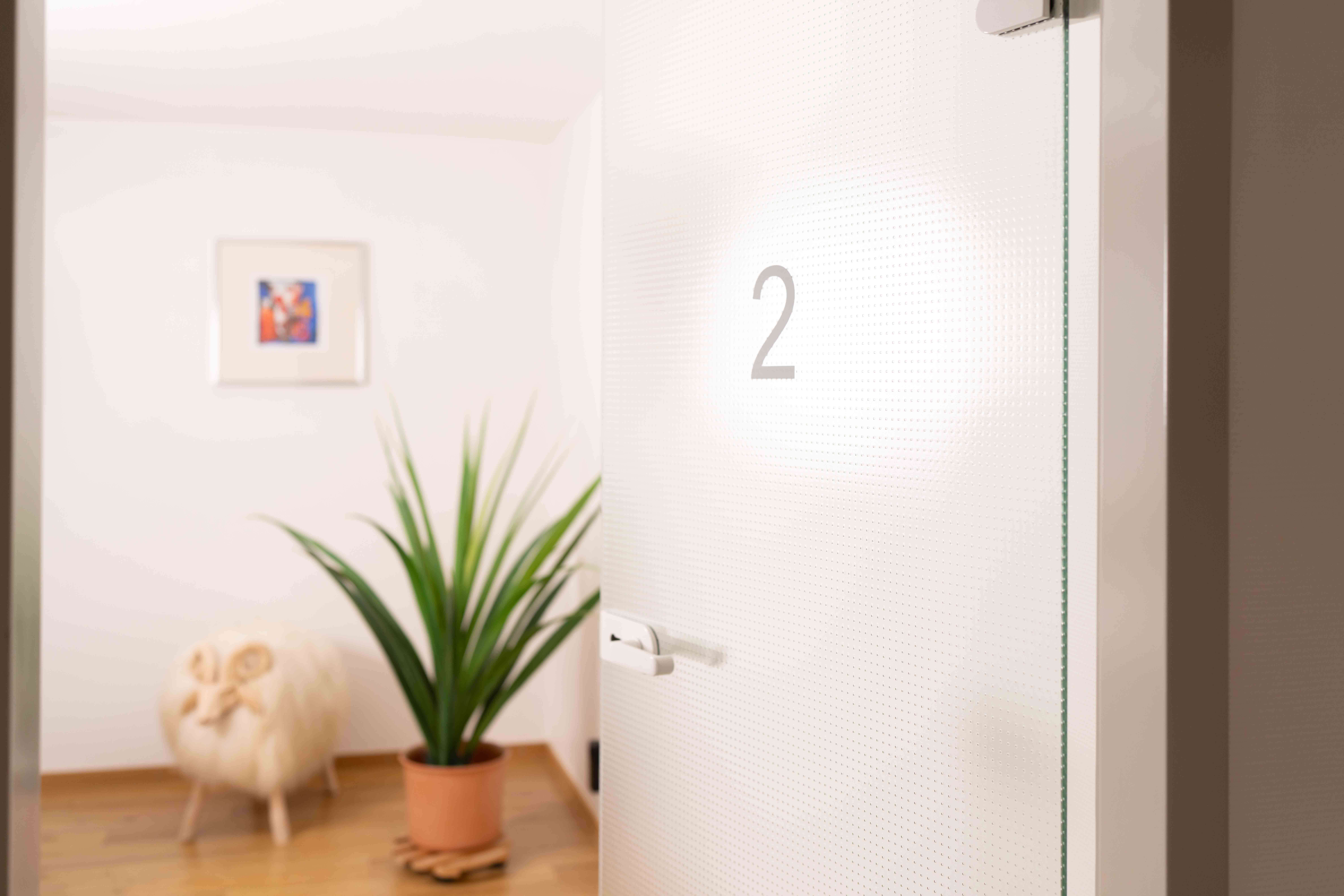 White door marked with number 2, with a potted plant and a decorative sheep figure blurred in the background.