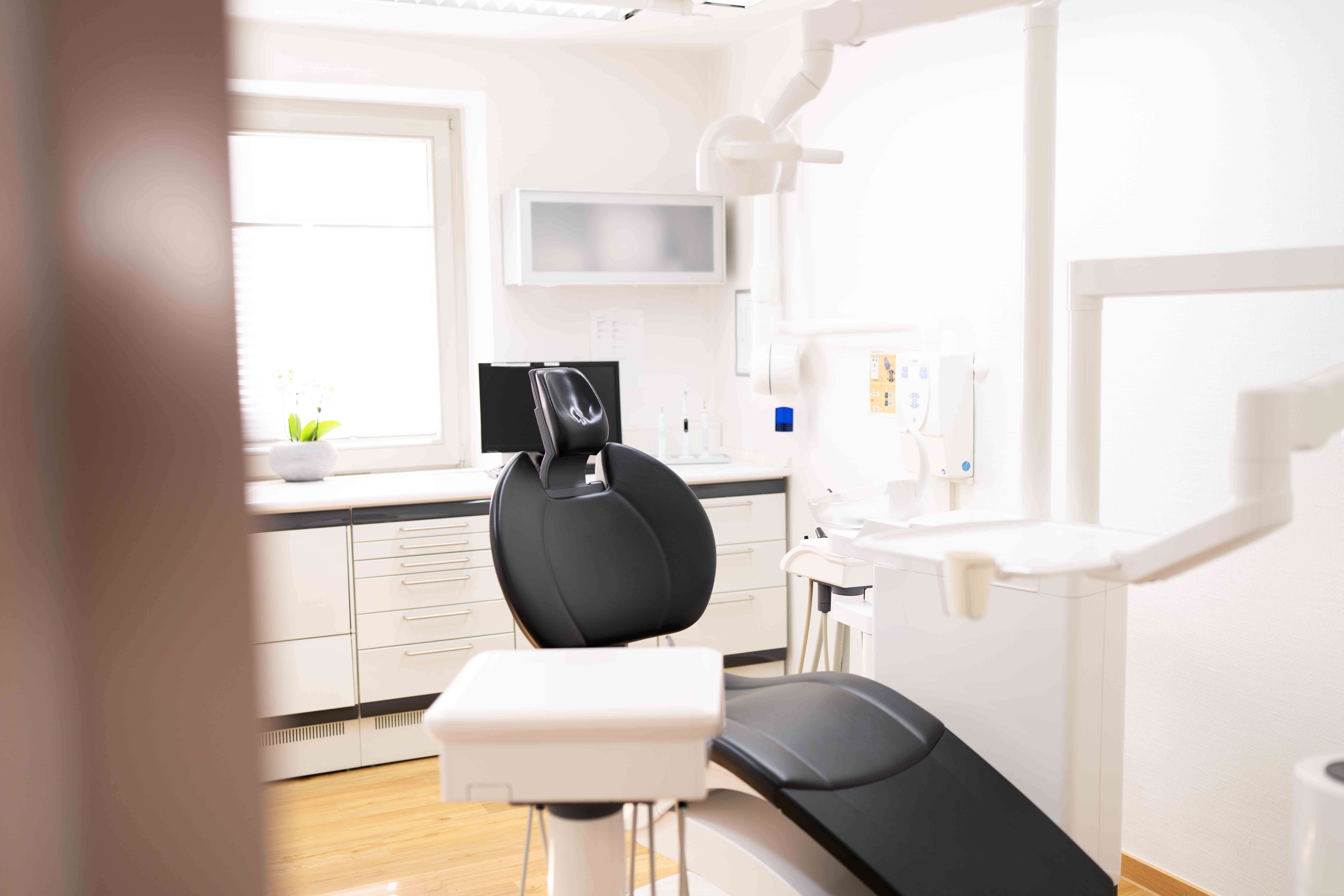 Modern dental examination chair in a bright clean dental office with cabinets and equipment.