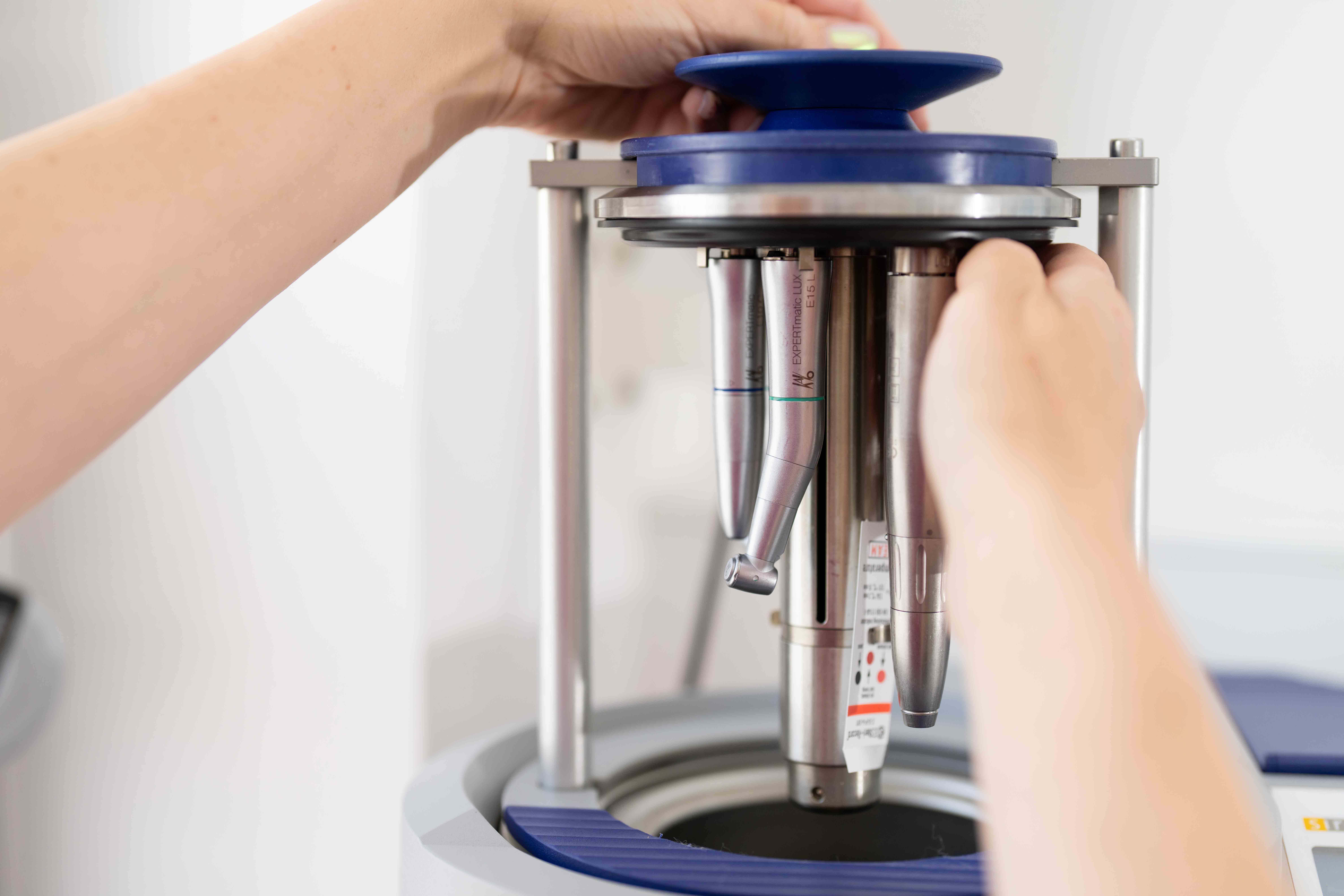 Hands adjusting dental handpiece attachments on a dental equipment holder.