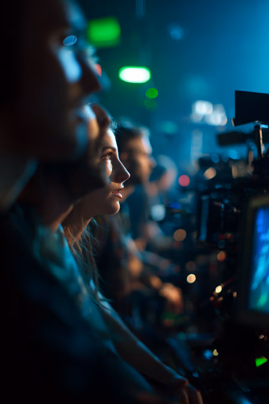 Profile of focused people seated closely in a dimly lit control room with screens and equipment.