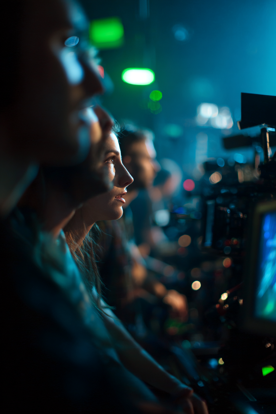 Profile of focused people seated closely in a dimly lit control room with screens and equipment.