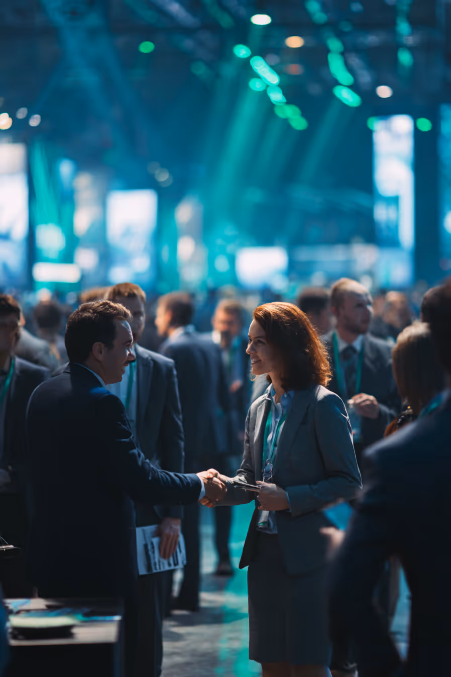 Two business professionals shaking hands and smiling at a crowded networking event.