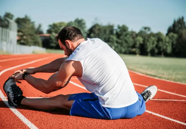 Athlete stretching on a red running track, demonstrating preparation for exercise and health principles