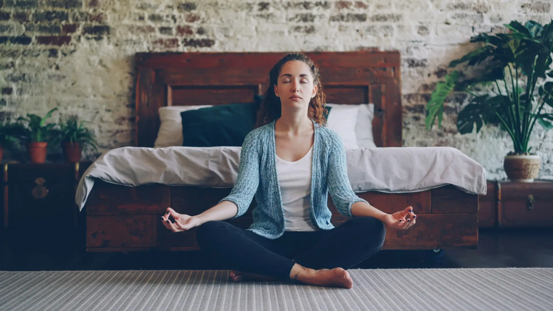 Eine Frau, die im Schneidersitz in einem Schlafzimmer meditiert und den Fokus auf mentale Gesundheit innerhalb der Hormonersatztherapie hervorhebt.