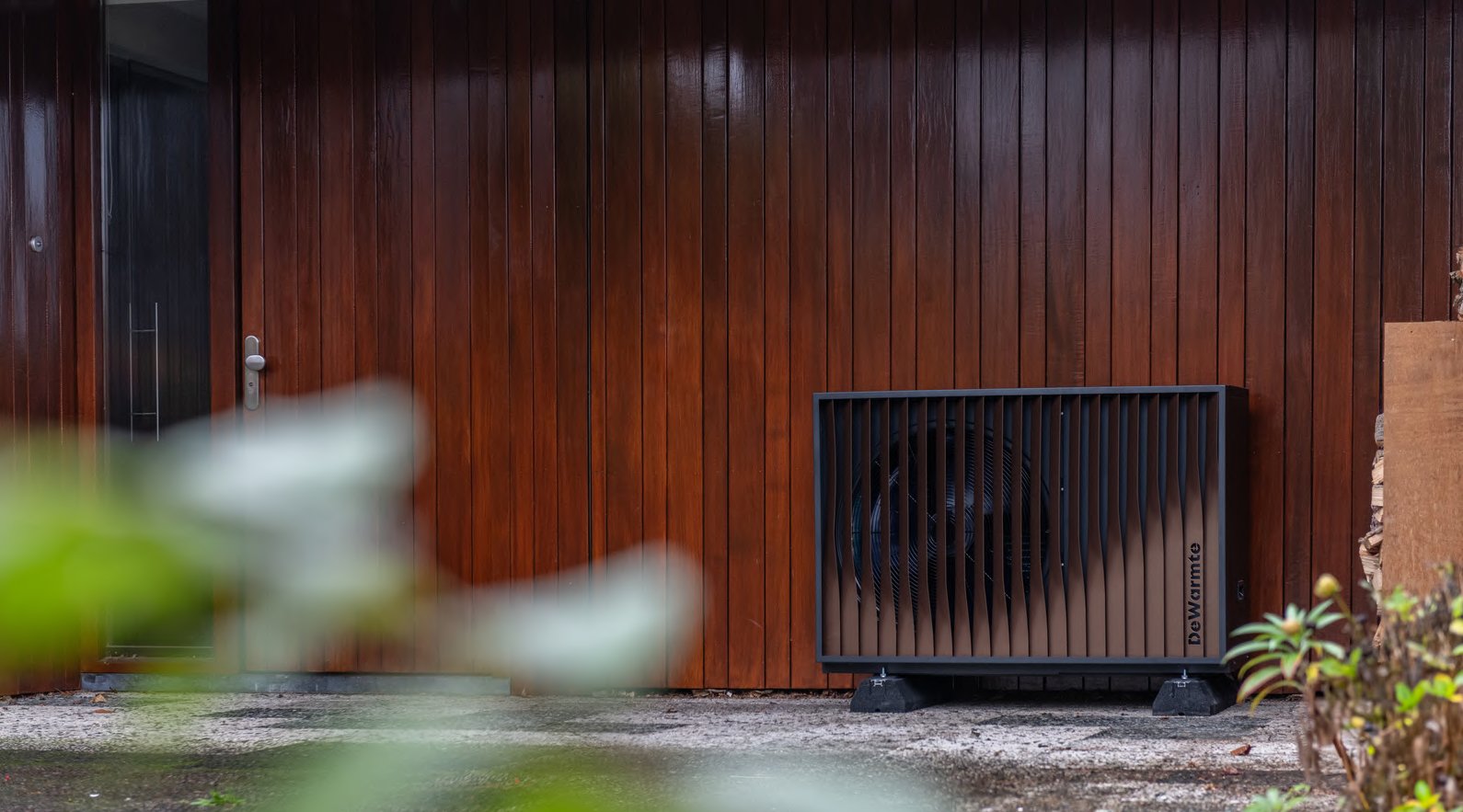 DeWarmte Pomp MP buitenunit voor een houten wand in de tuin