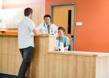 Doctor and receptionist assisting a patient at a healthcare front desk