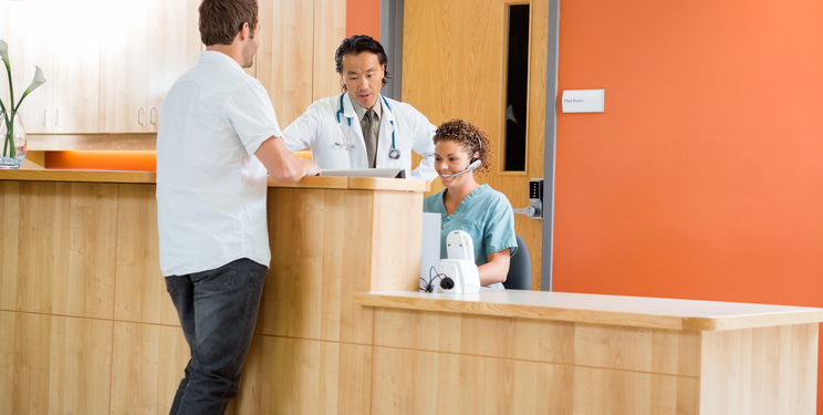 Doctor and receptionist assisting a patient at a healthcare front desk